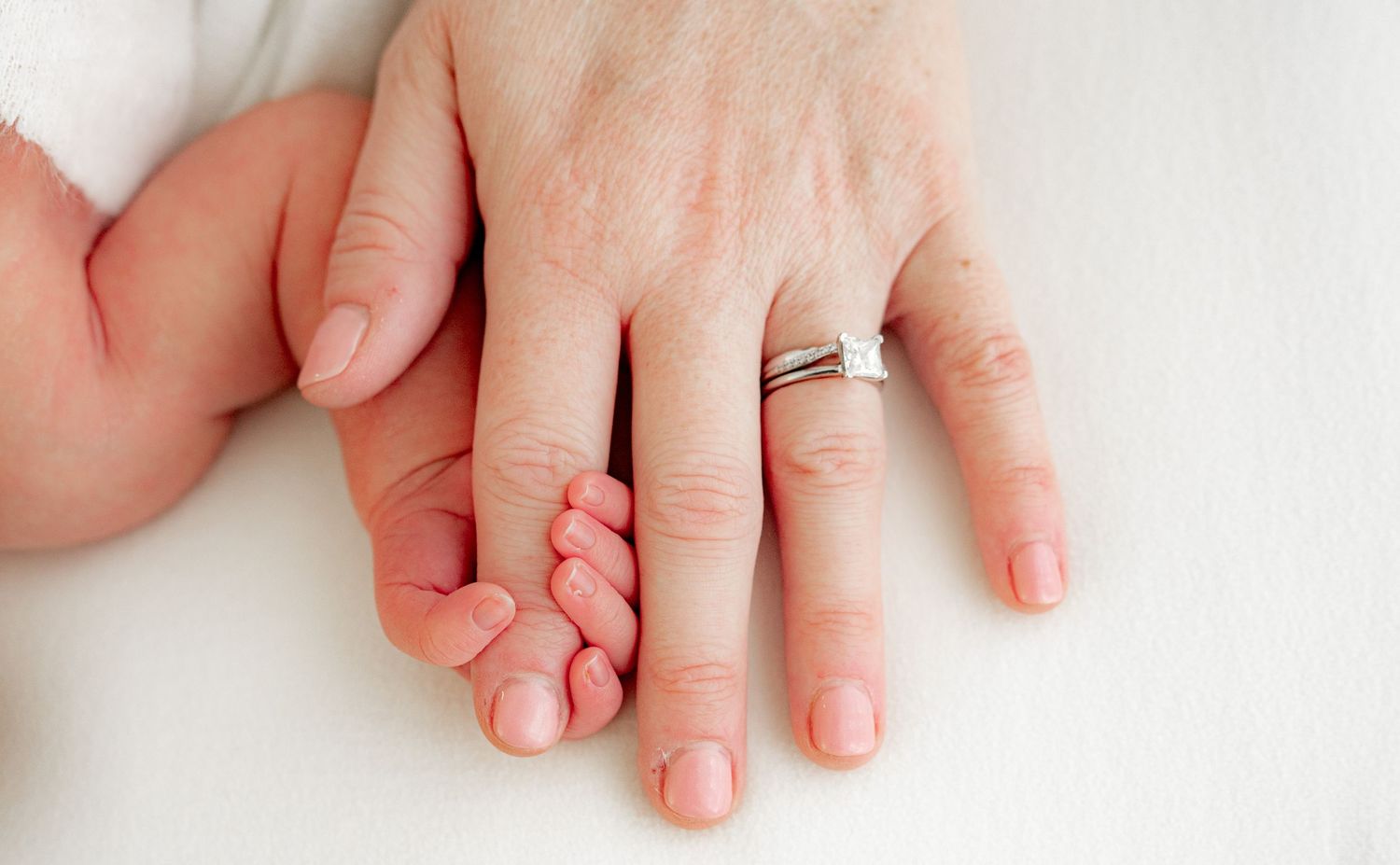 Detail shot of a mother's hand, with their finger wrapped around their baby's fingers.