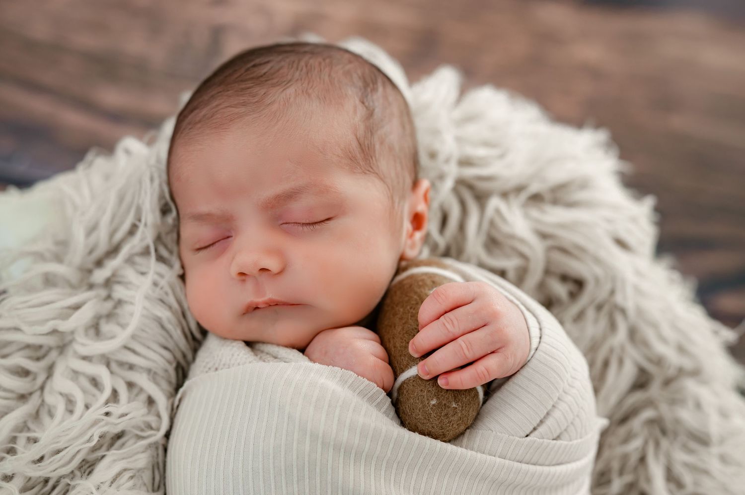 Wrapped, sleeping newborn holding a football during his Katy, TX newborn studio session.