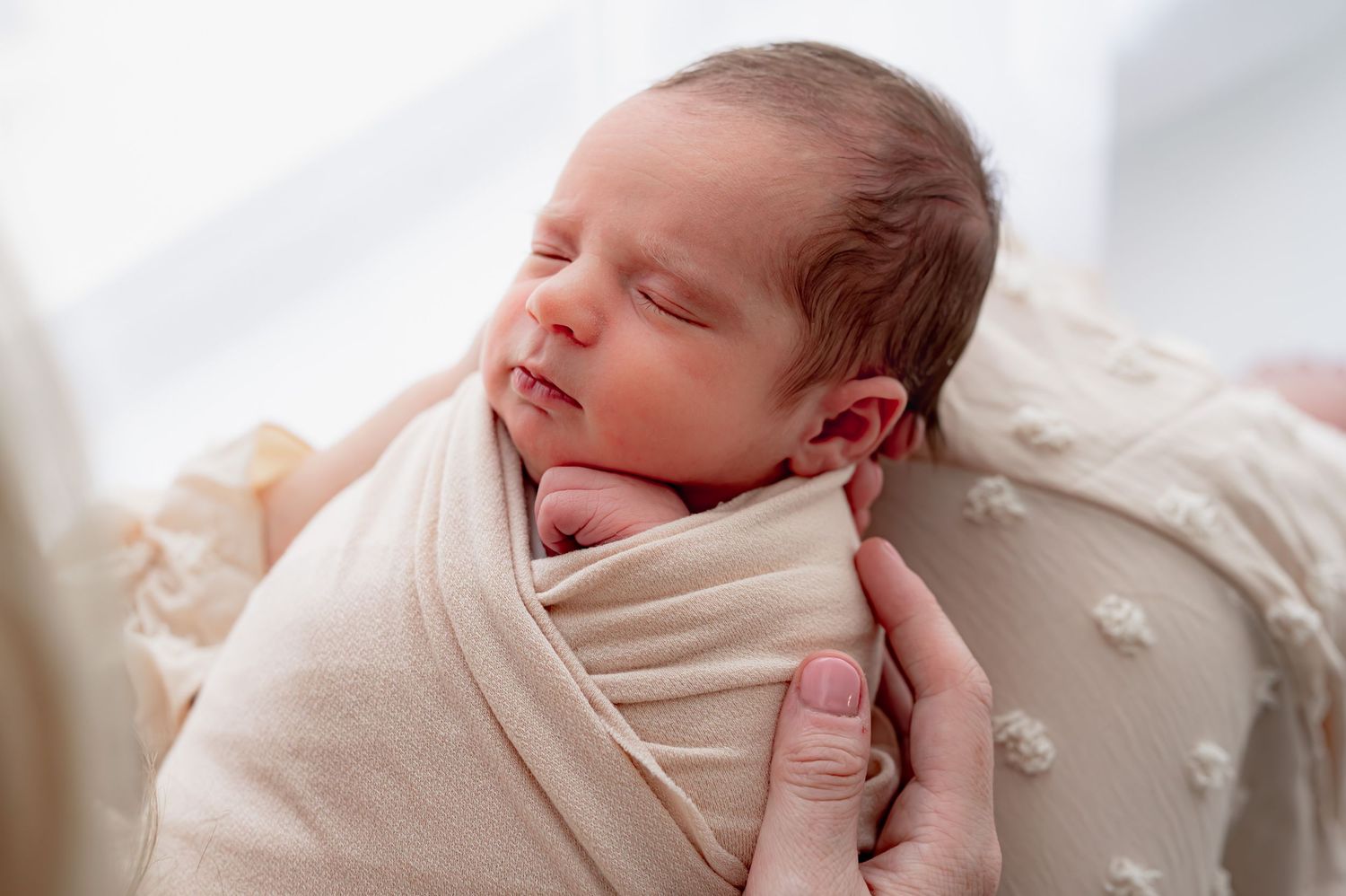 Newborn baby swaddled in a cream blanket and resting in her mother's arms.