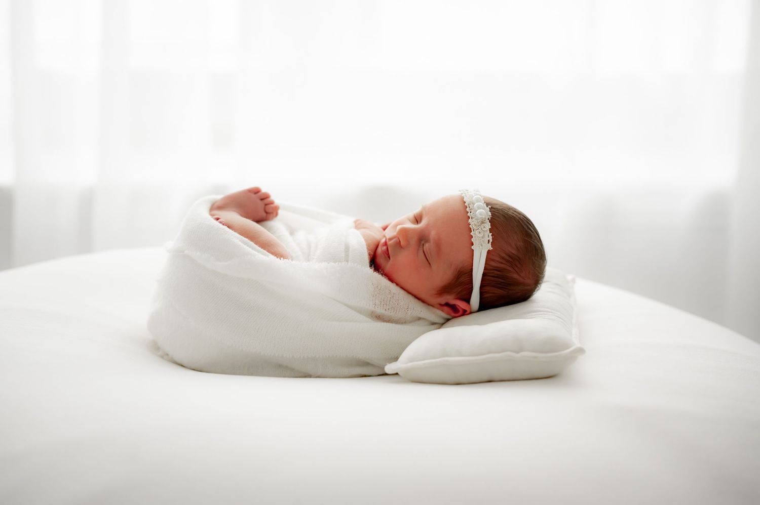 Newborn wrapped in white and resting on a small pillow.