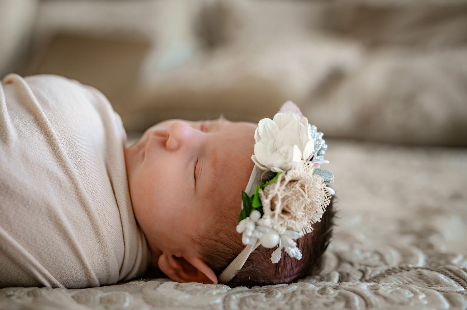 Side view of a sleeping newborn wrapped in cream with a floral headband.