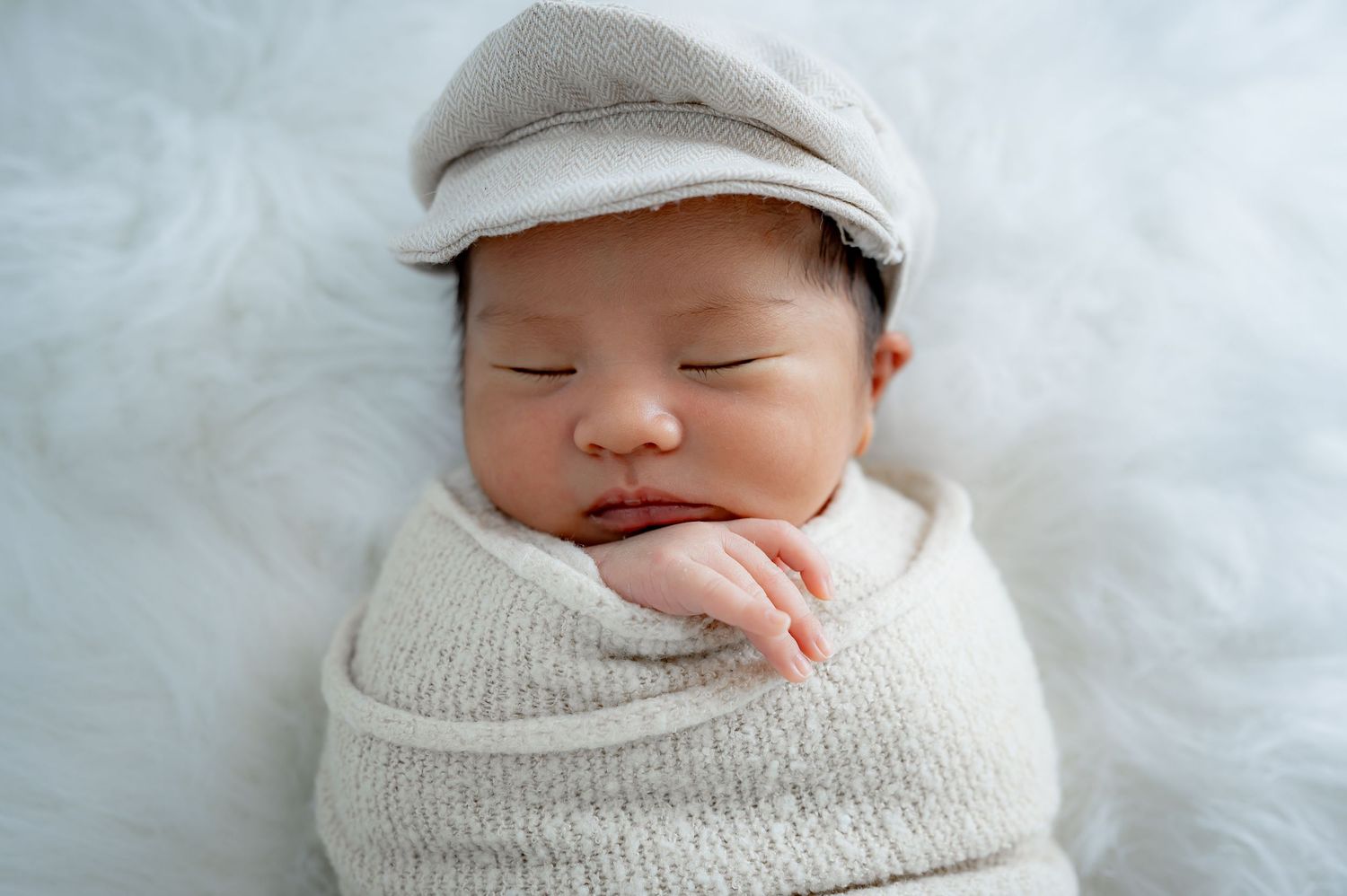 Wrapped newborn baby wearing neutral tones during studio session in Fulshear Tx