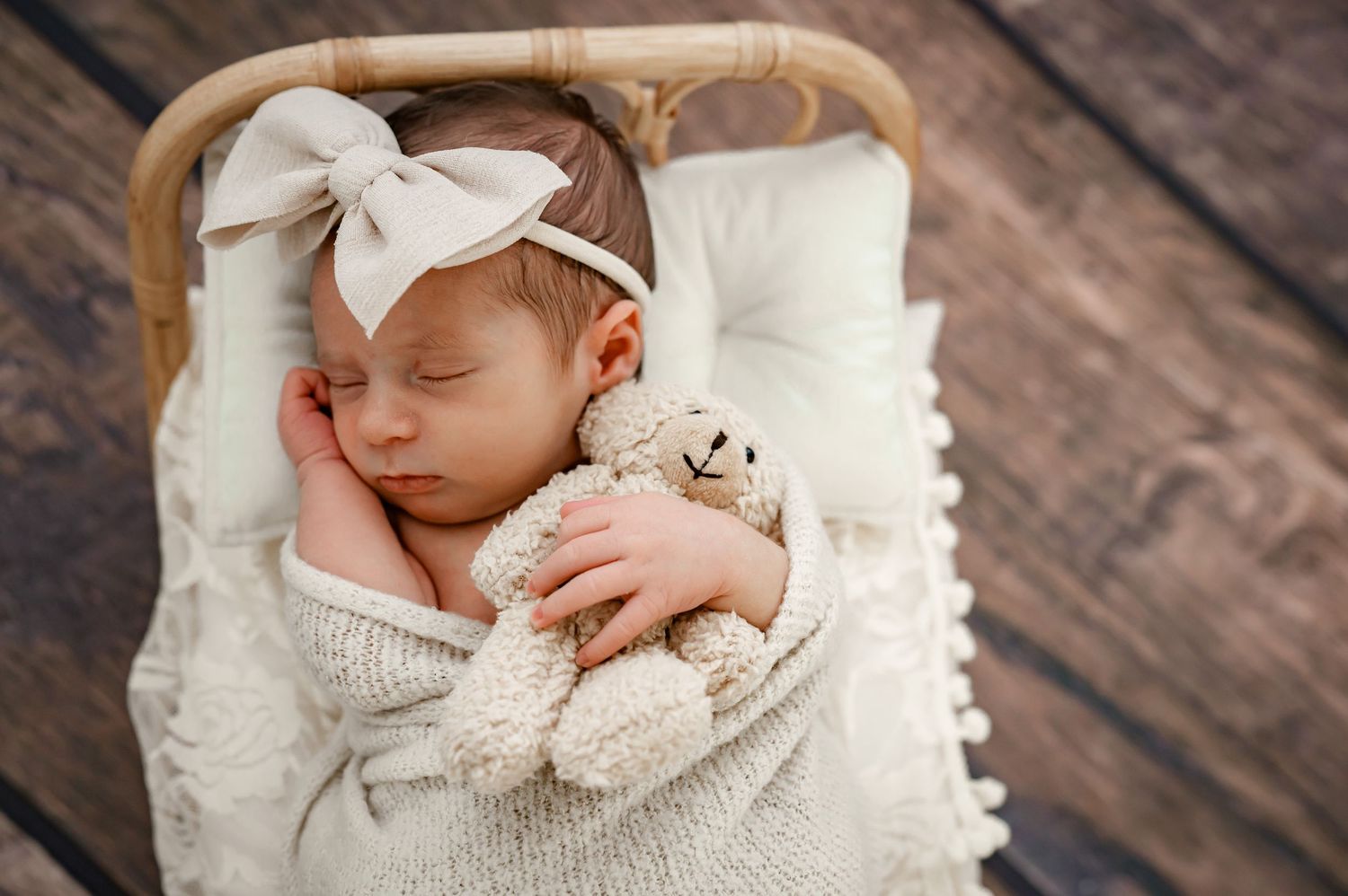 Sleeping baby wearing a white bow headband and holding a small teddy bear.