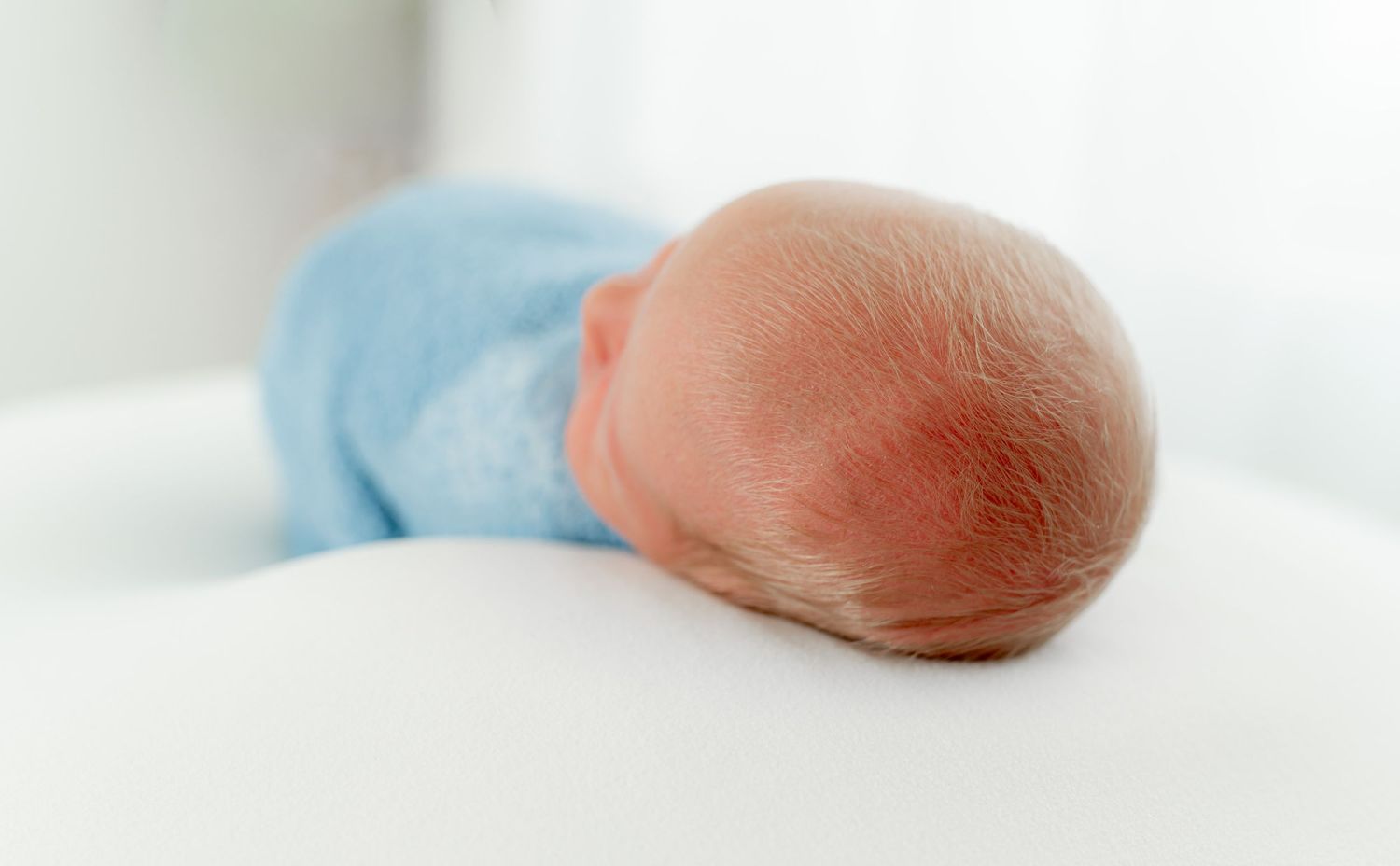 Close-up of a newborn baby wrapped in blue, resting on a white blanket.