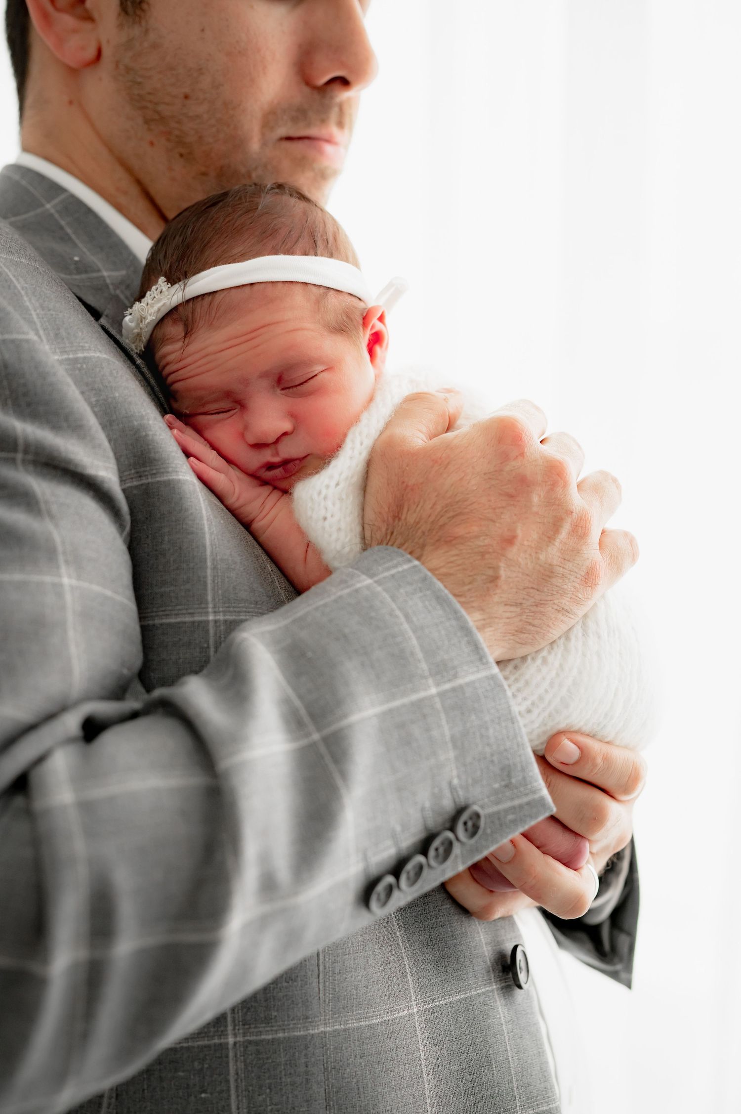 Newborn baby resting against their father's chest as he holds her in his arms.