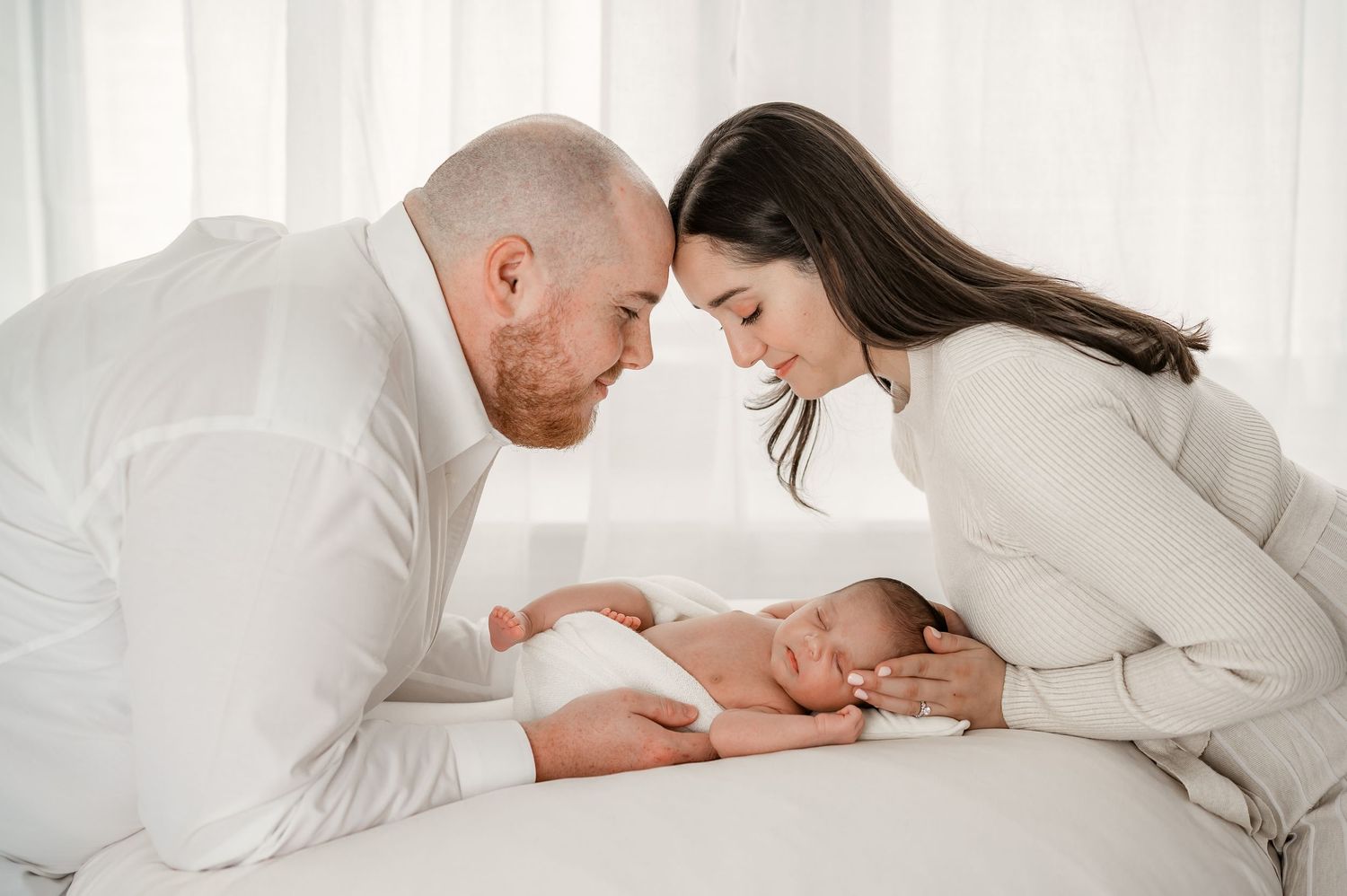 Parents share an intimate moment gazing at their sleeping newborn during their Katy studio newborn session.