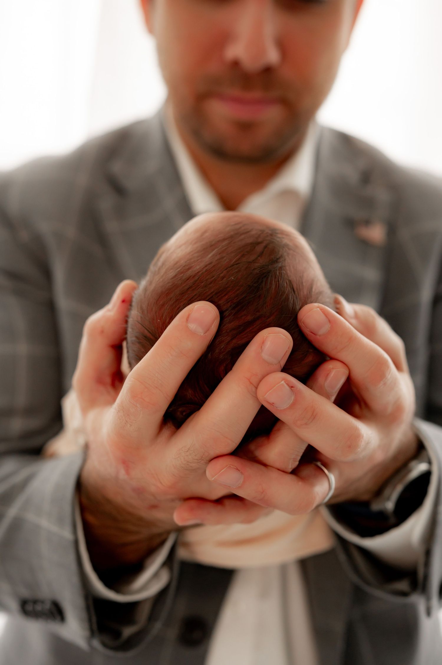 Father gently cradling his newborn baby's head in both hands.