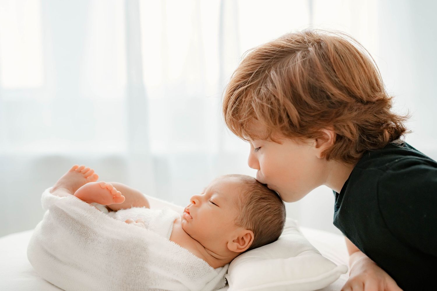 Emotional newborn photo of sibling kissing baby during Katy newborn session.