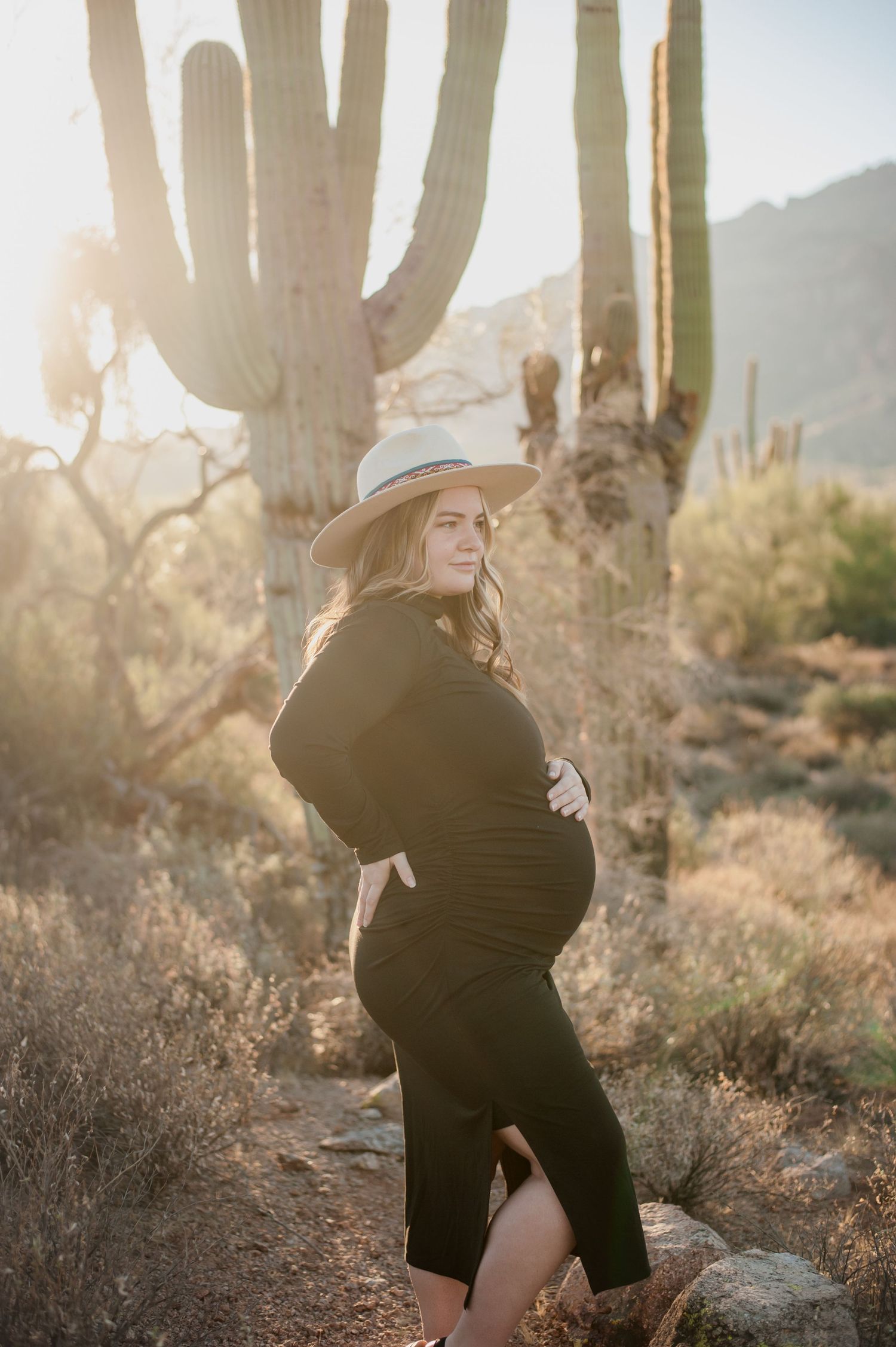Romantic couple embraces in a desert landscape with tall saguaro cacti and golden sunlight at sunset.