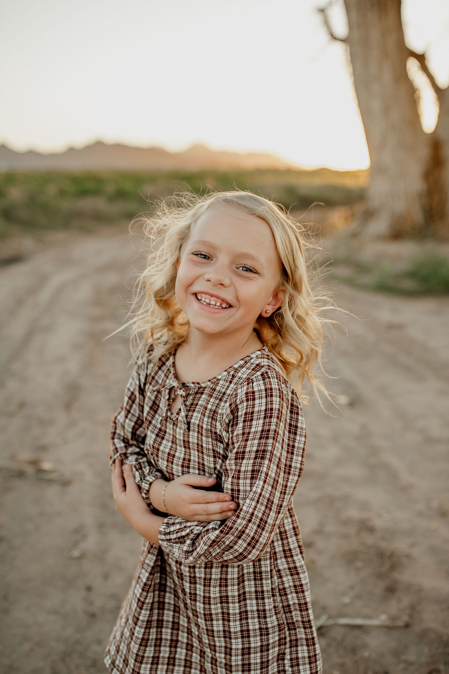 Three candid photos of a child in a plaid dress laughing and playing outdoors during golden hour.
