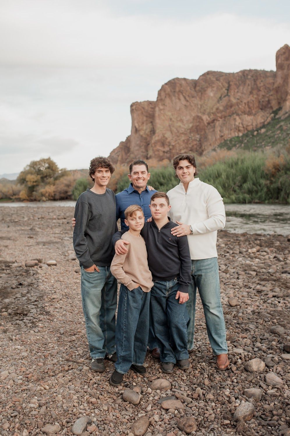 Family of five posing outdoors near a rocky riverbank with red cliffs in the background.