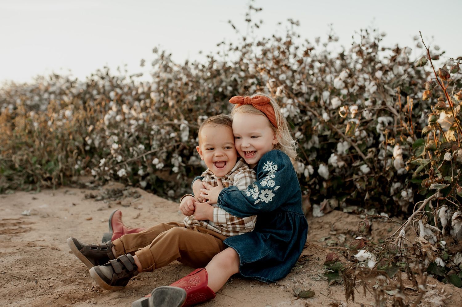 Two happy children hugging and laughing together in a cotton field during a fall family photo session.