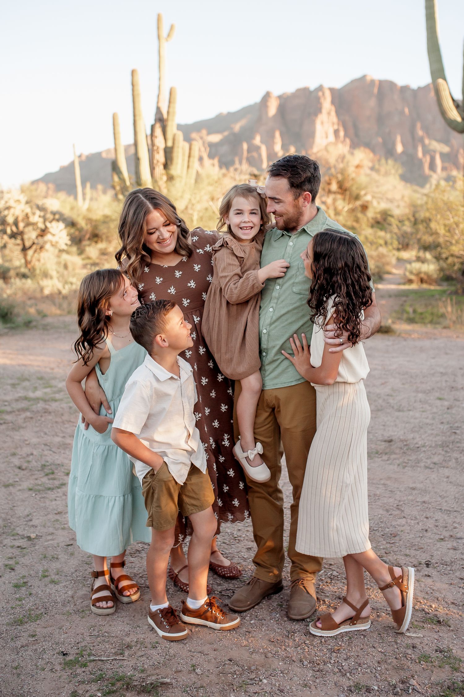 Family of six posing together in Arizona desert with saguaro cacti and mountain backdrop during golden hour.