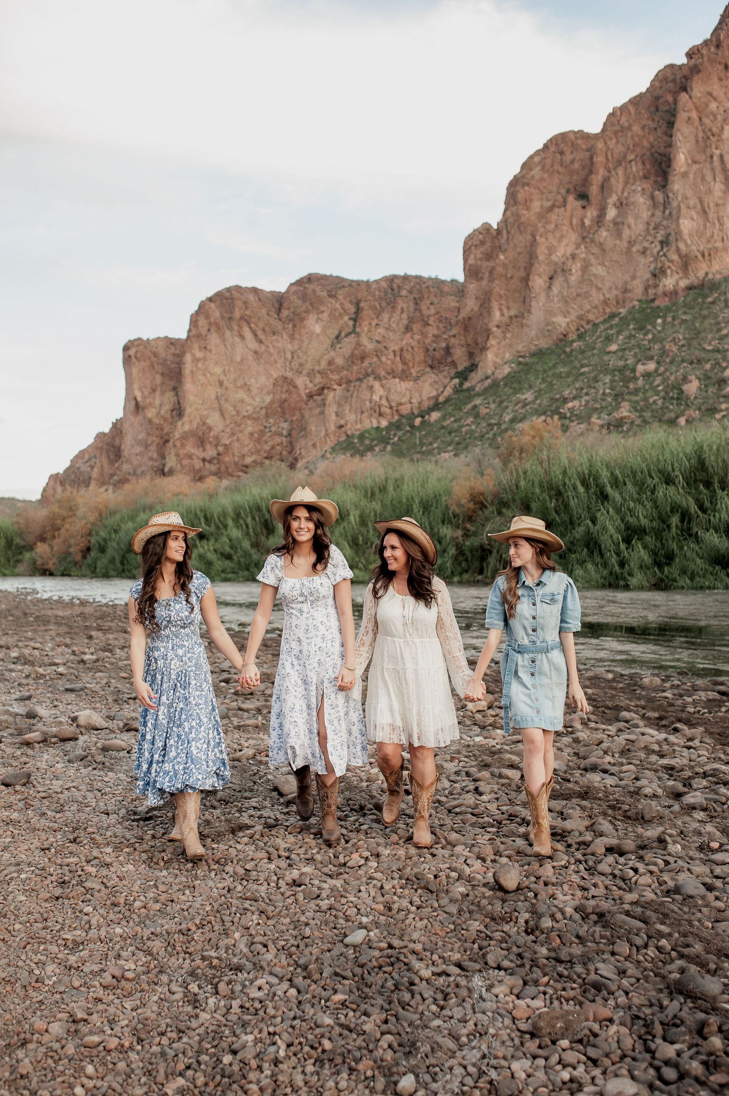 Group walking together on rocky riverbank with dramatic desert cliffs towering in the background.