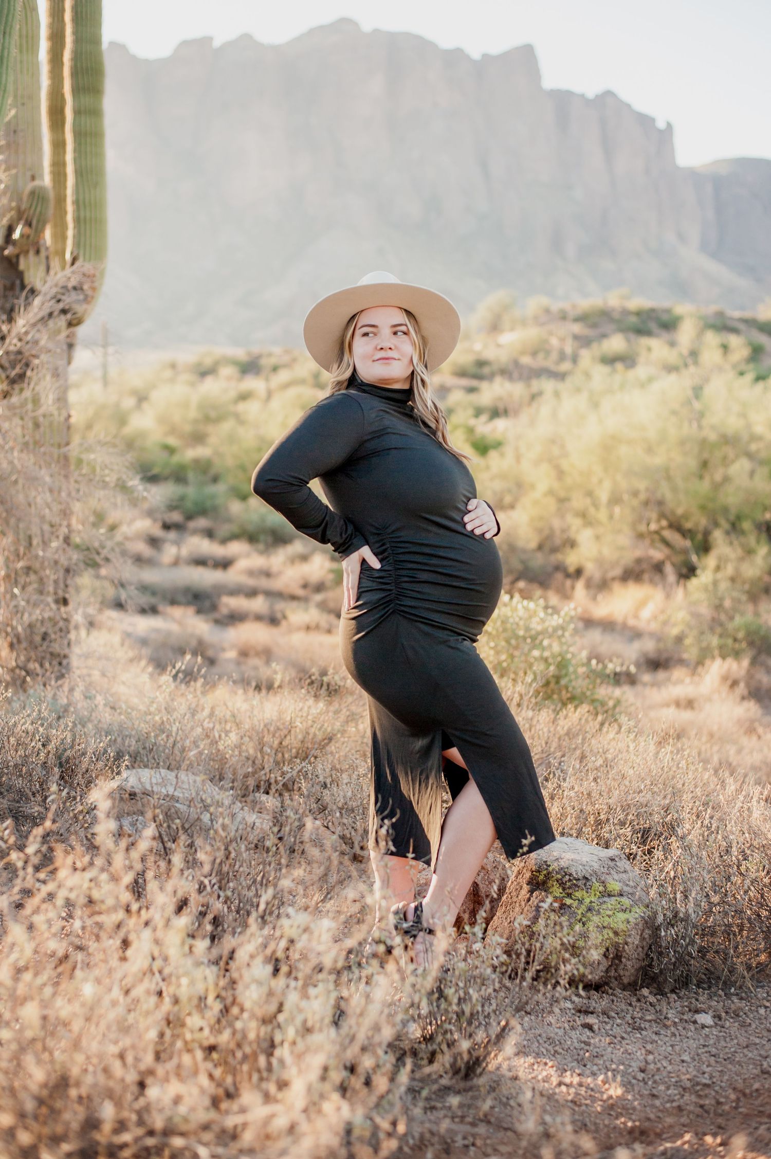 Desert maternity portraits showing candid moments against rugged mountain backdrop with desert brush and cacti.
