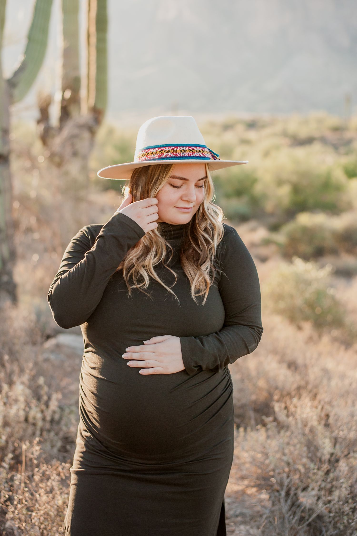 Maternity photoshoot in a desert landscape with saguaro cacti and mountains in the background at golden hour.