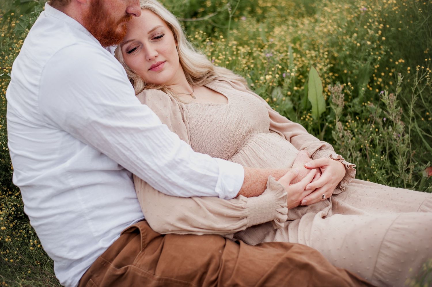 A couple in white and beige outfits embrace in a sunny meadow during a romantic photoshoot.