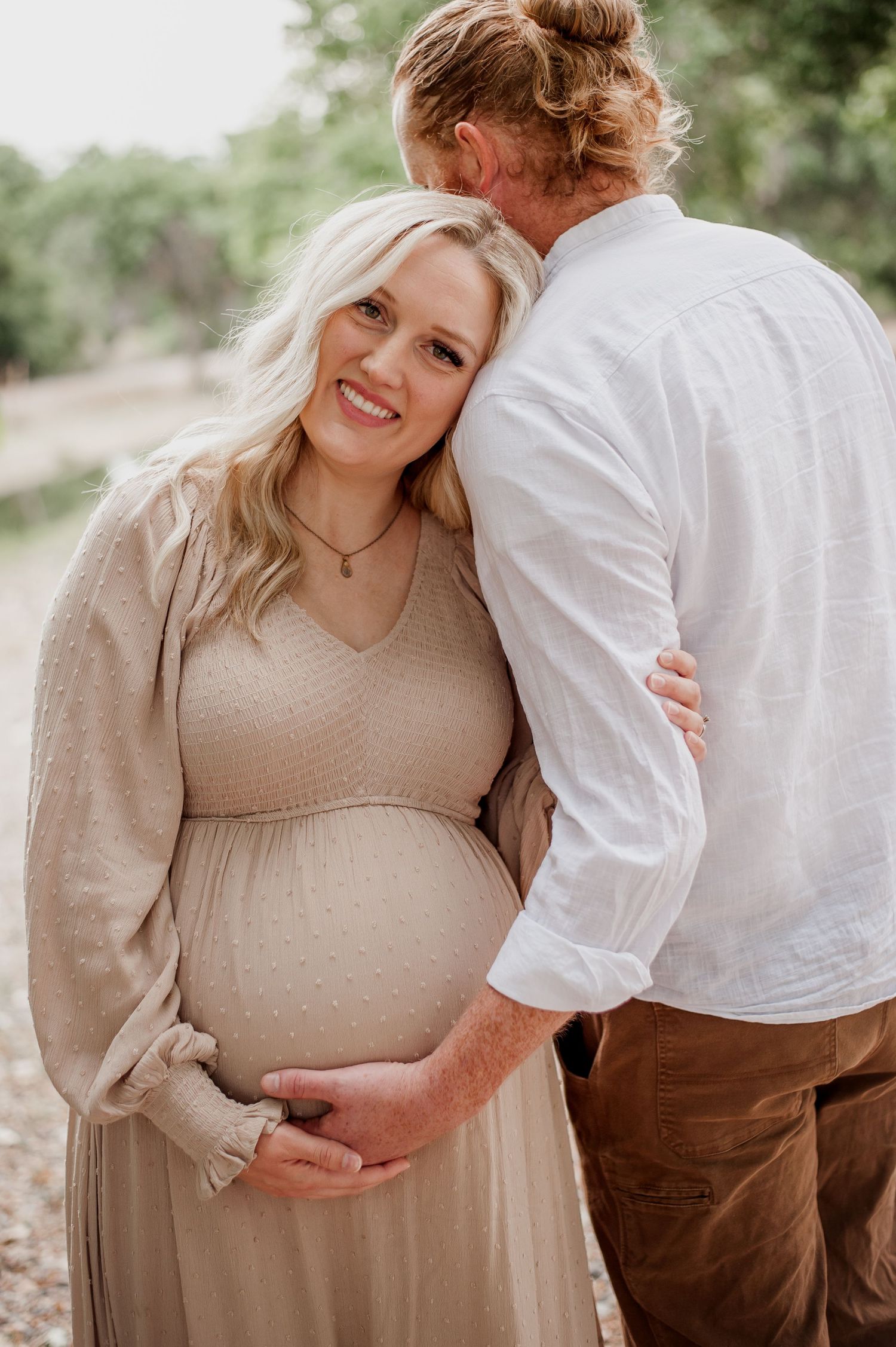 Expecting parents embrace tenderly during an outdoor maternity photography session in natural lighting.