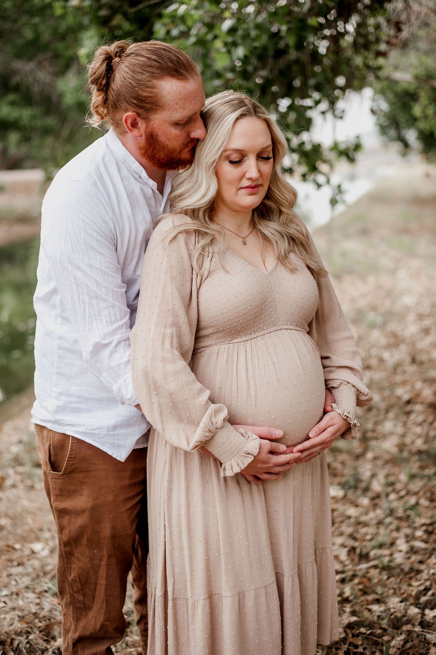 An intimate maternity photo session outdoors with a couple in beige and brown clothing.