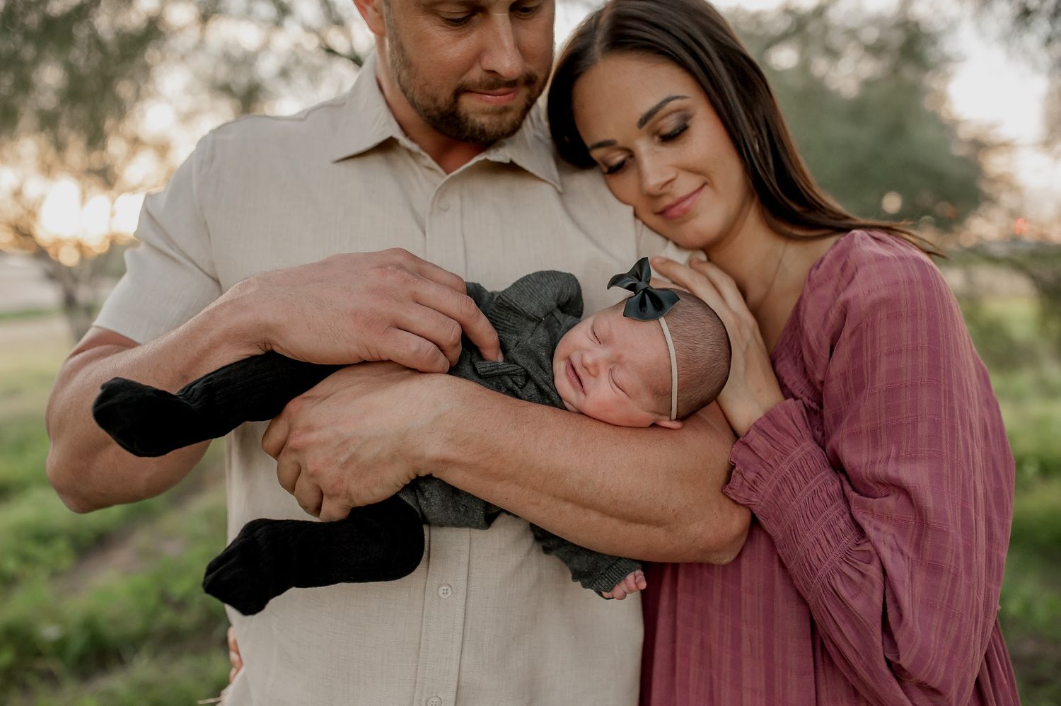 A couple tenderly cradles their newborn baby outdoors during a golden hour family portrait session.