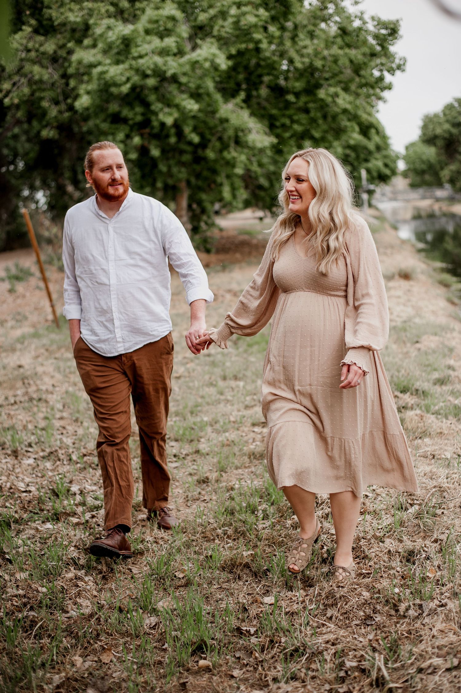 A couple in neutral tones walks through a rustic outdoor setting during a romantic photoshoot.