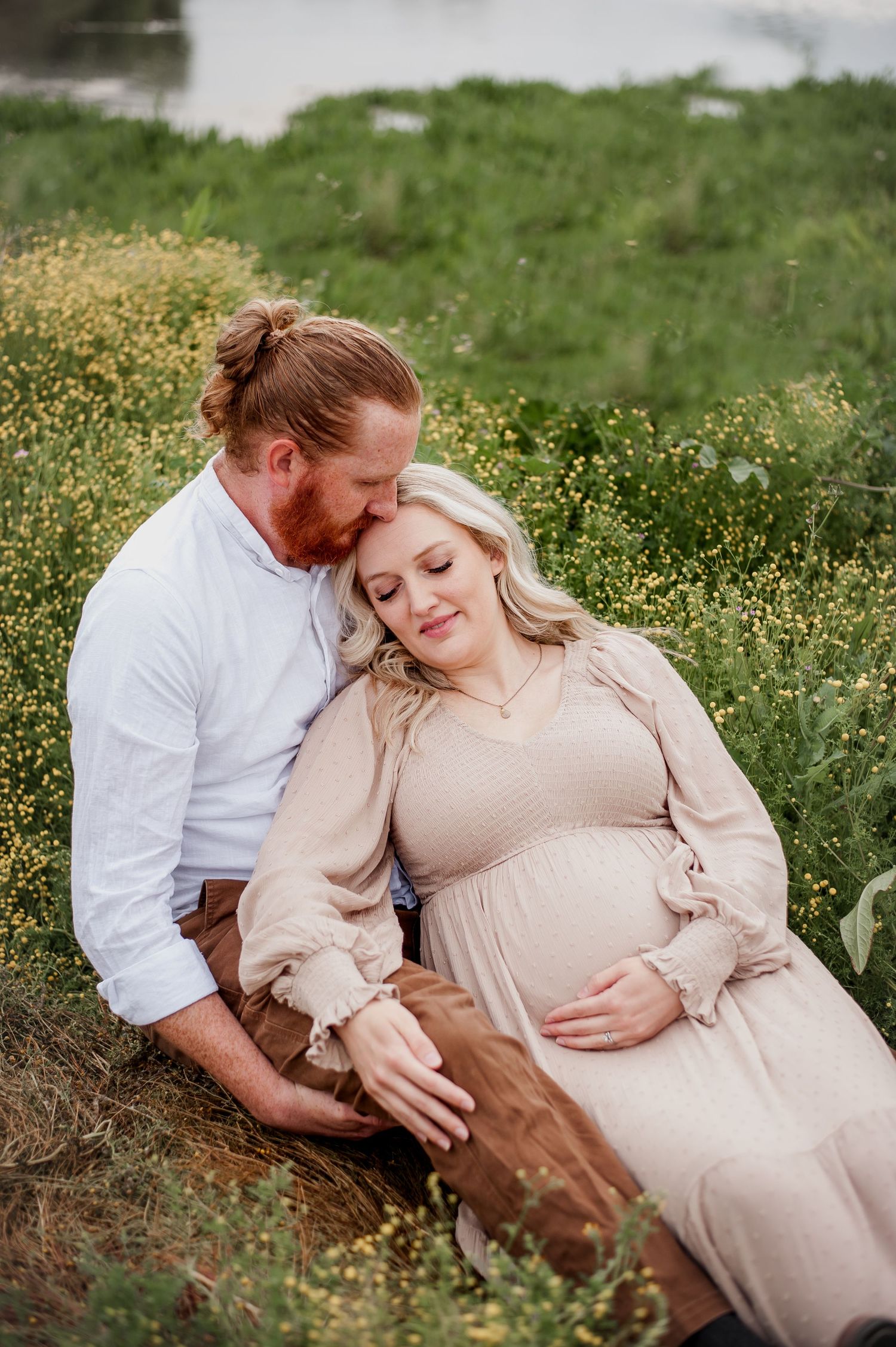 A couple shares an intimate moment outdoors in a field of wildflowers during a maternity photoshoot.