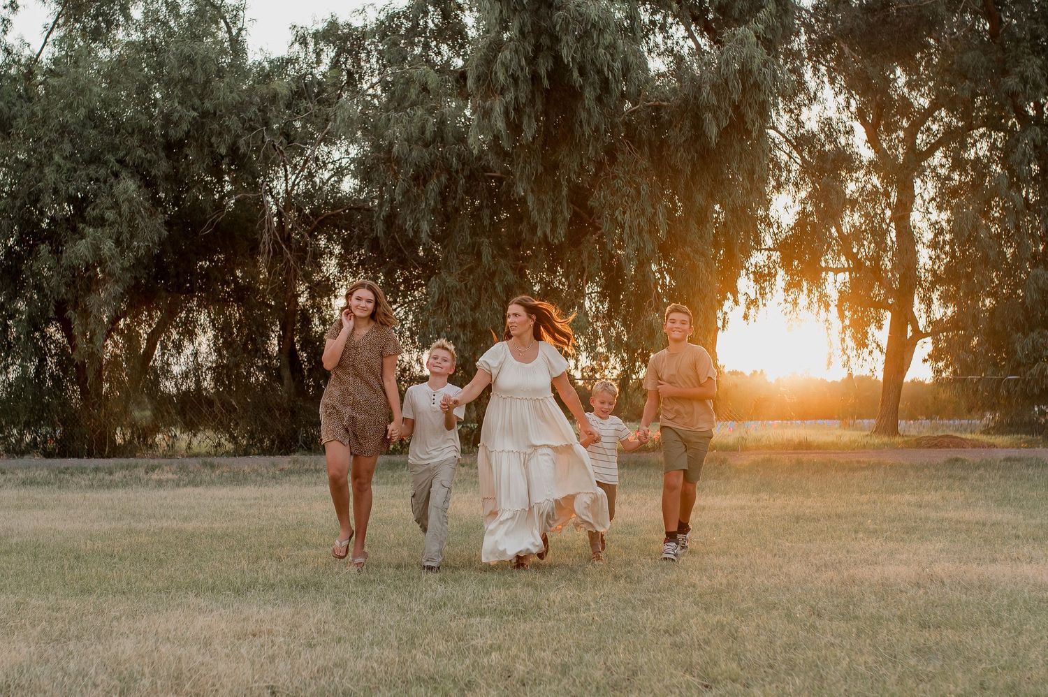 Family running joyfully through a sunlit park at golden hour with trees in the background.