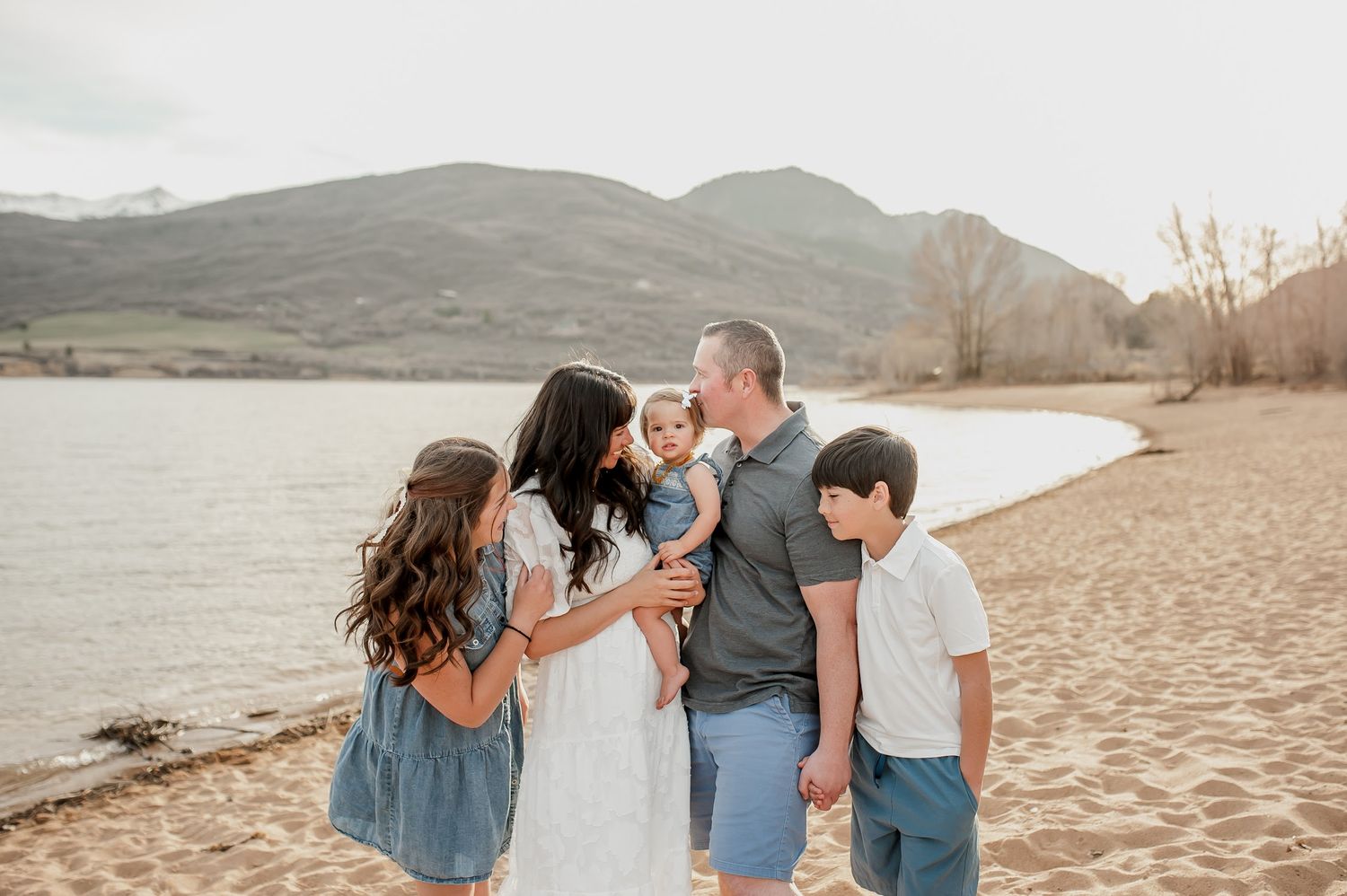 Family of five sharing a joyful moment on a sandy beach with mountain backdrop in warm natural light.