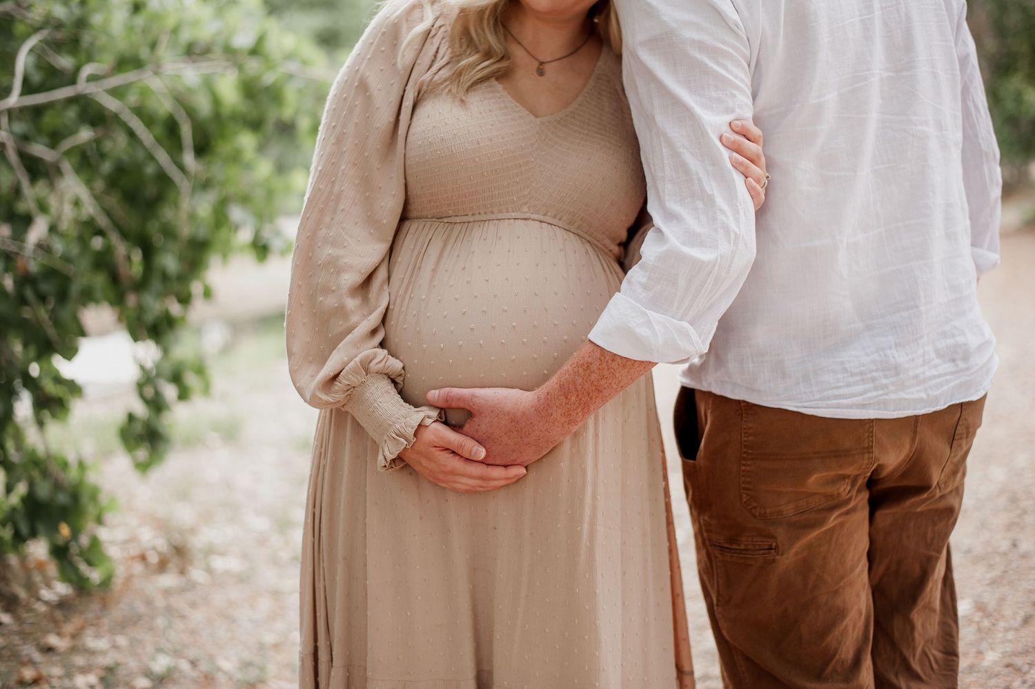 A close up shot showing hands cradling a pregnant belly in a beige dress.