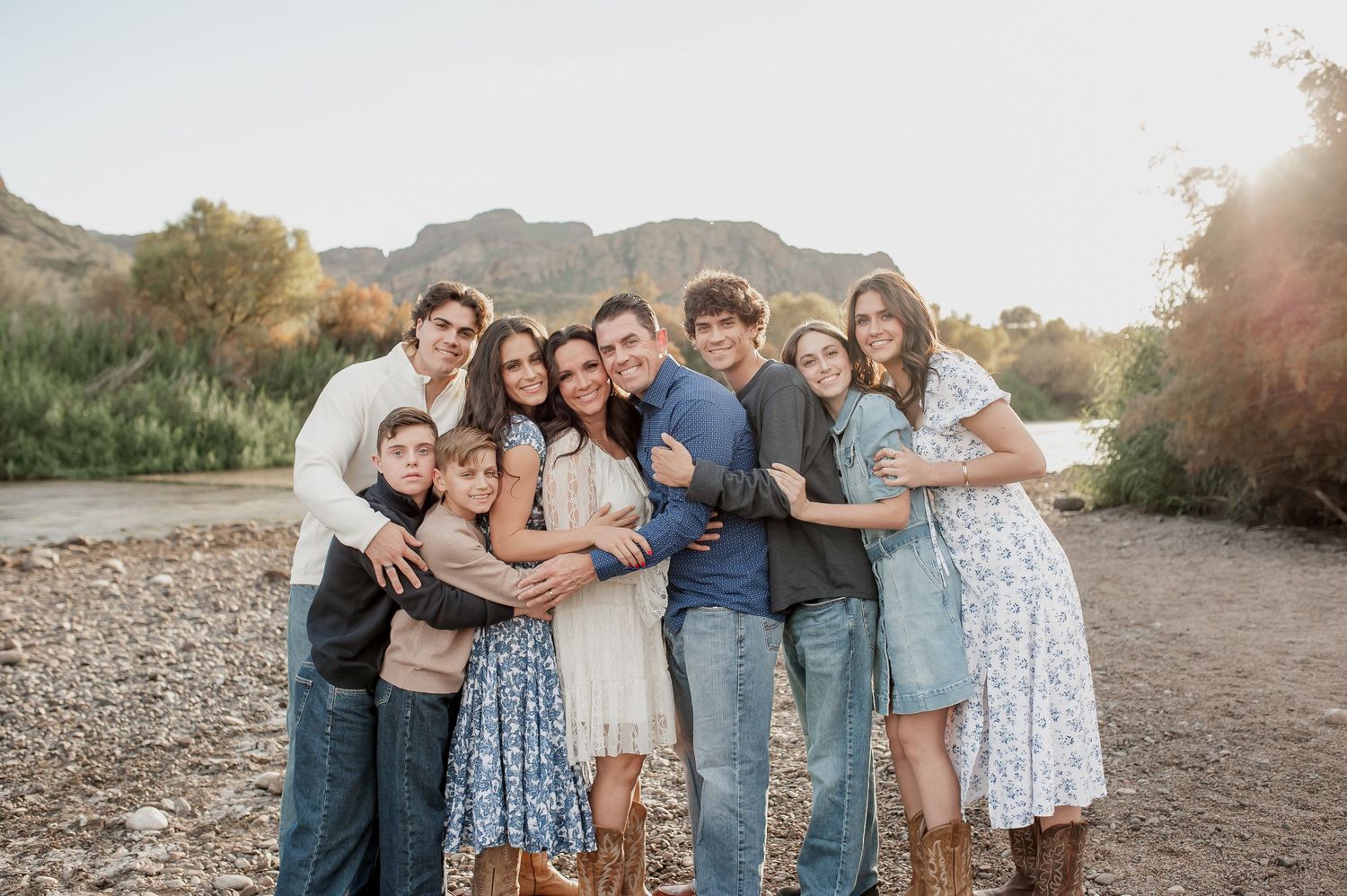 A group poses together outdoors at sunset in coordinated blue and white outfits for a casual family photo session.
