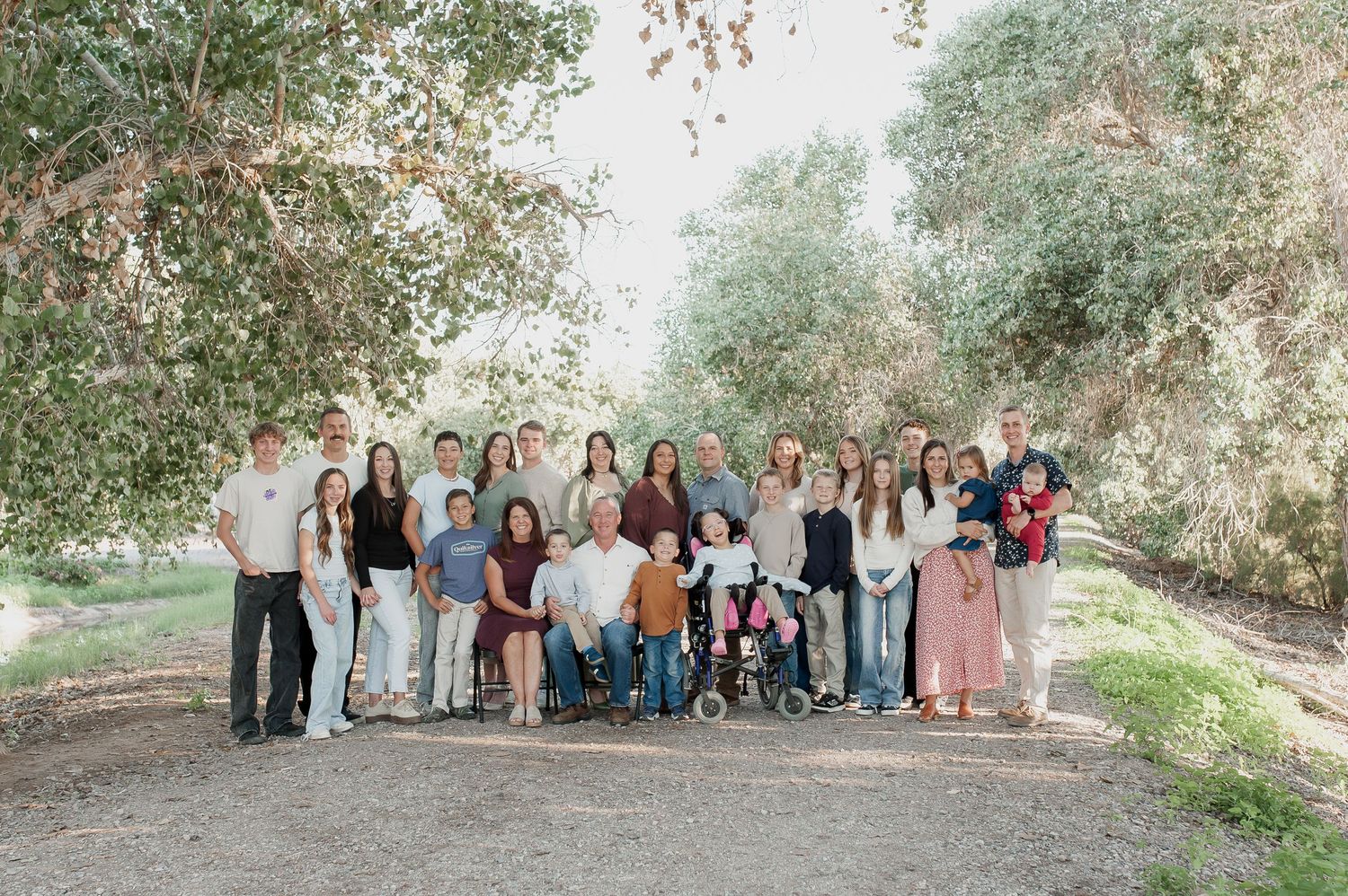 Large family group poses outdoors for casual portrait session in natural wooded setting.
