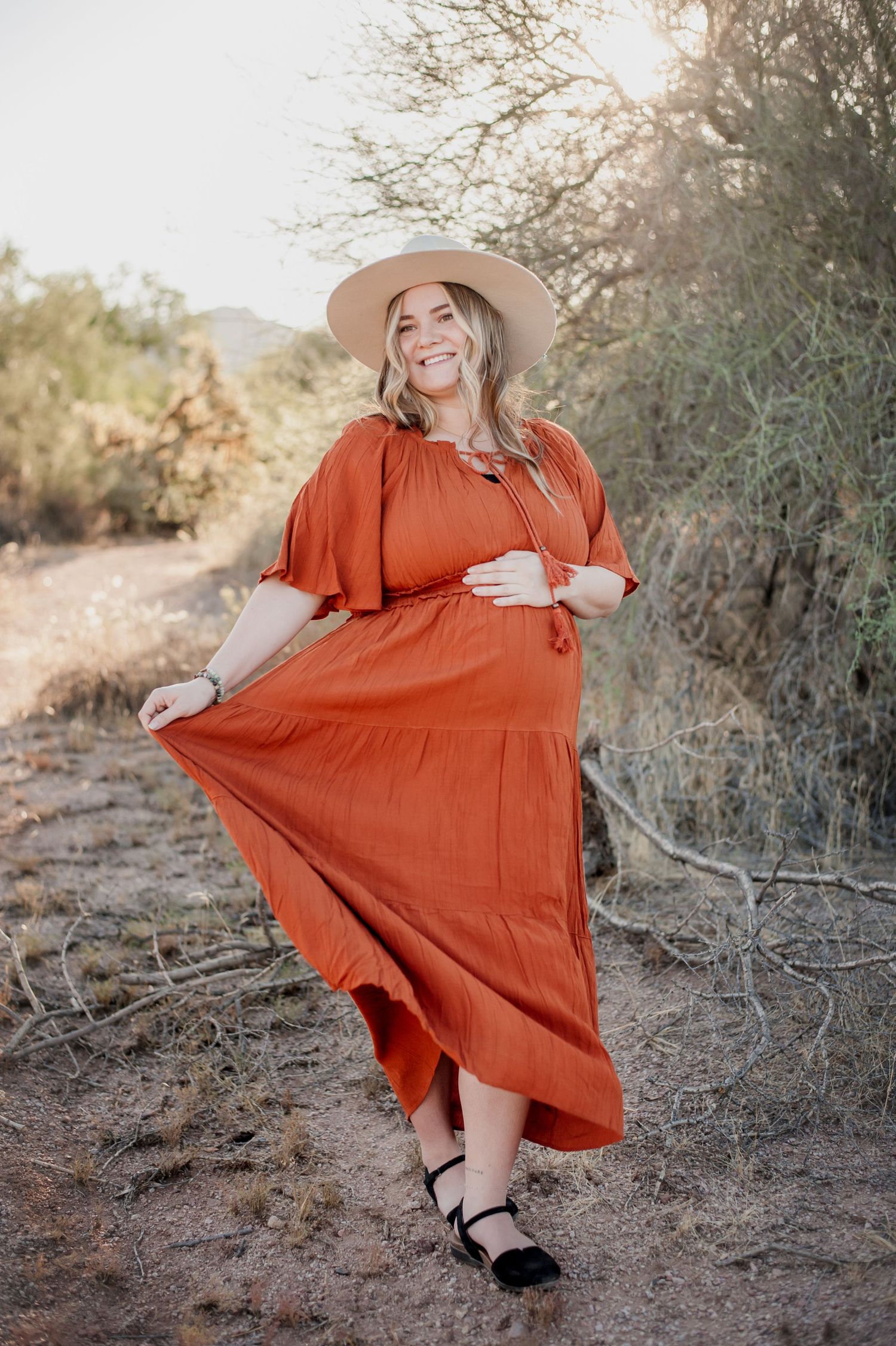 A flowing rust-colored maxi dress with ruffled tiers and a wide-brimmed hat creates a romantic desert photoshoot look.