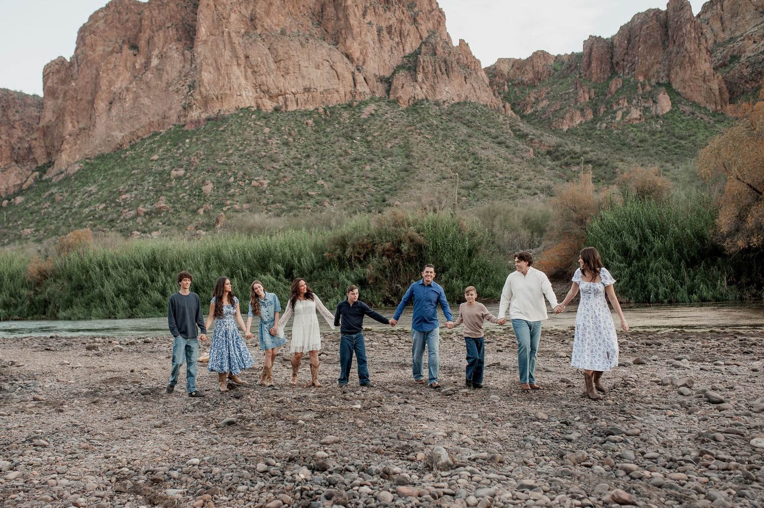 A group of people stand together against a backdrop of towering red rock cliffs in a desert landscape.
