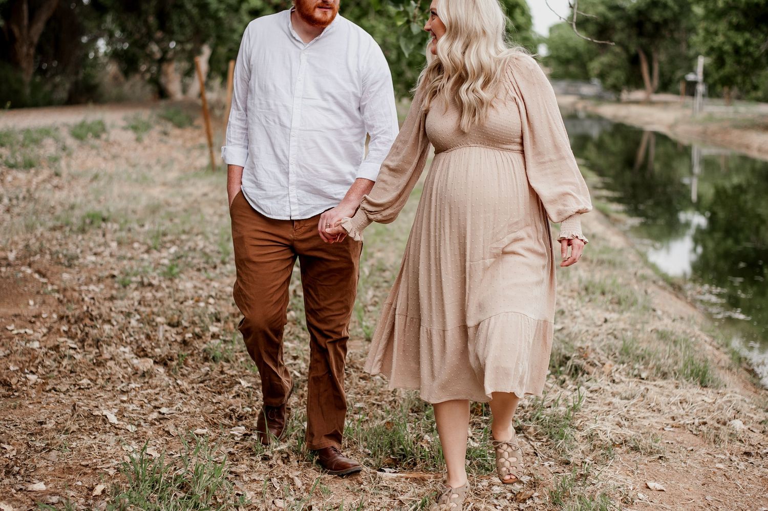A couple walks together on a gravel path wearing coordinated earth-toned outfits in a romantic outdoor setting.