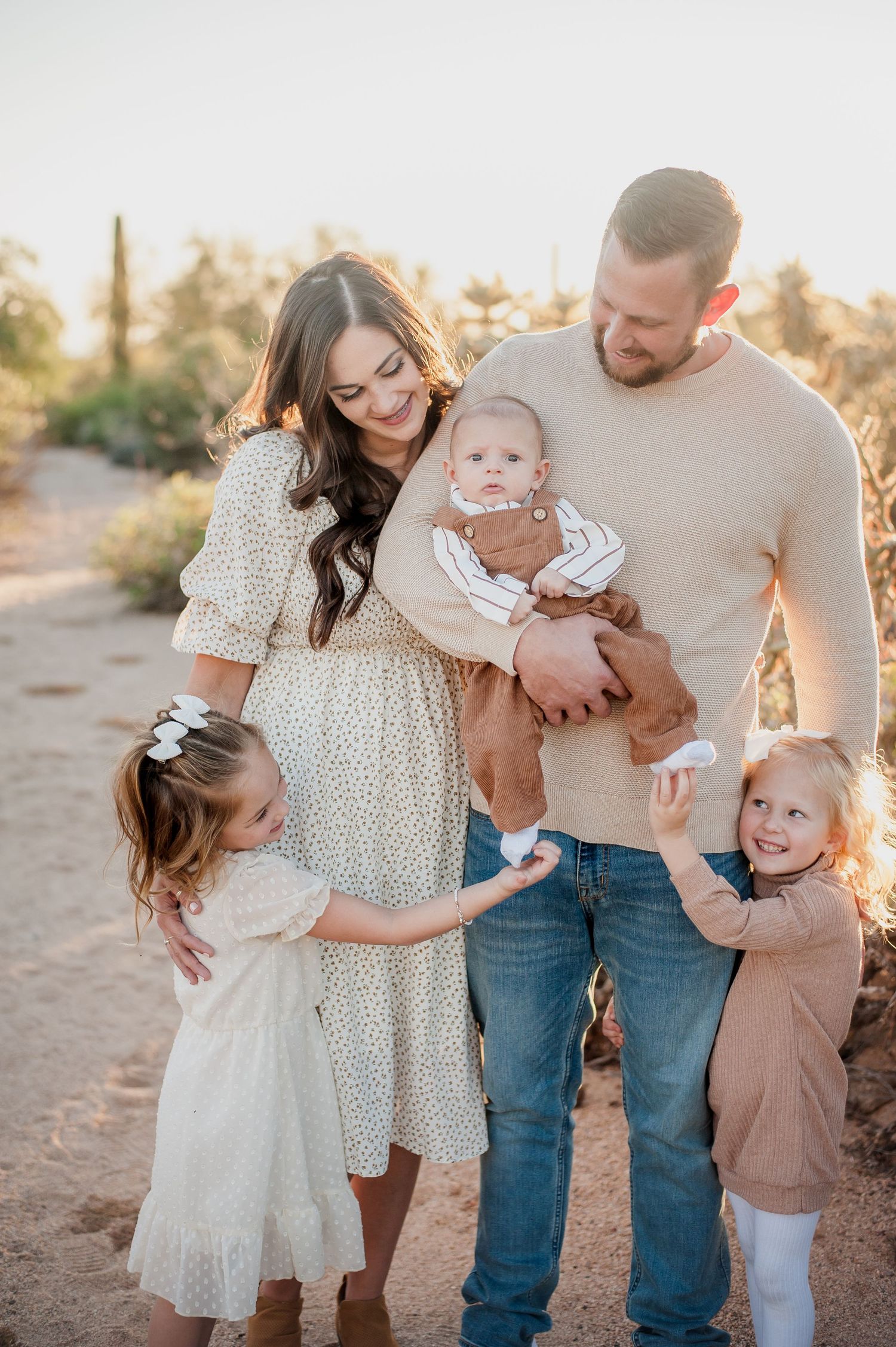 Happy family of five posing outdoors in desert setting, parents with three young children in warm neutral tones.