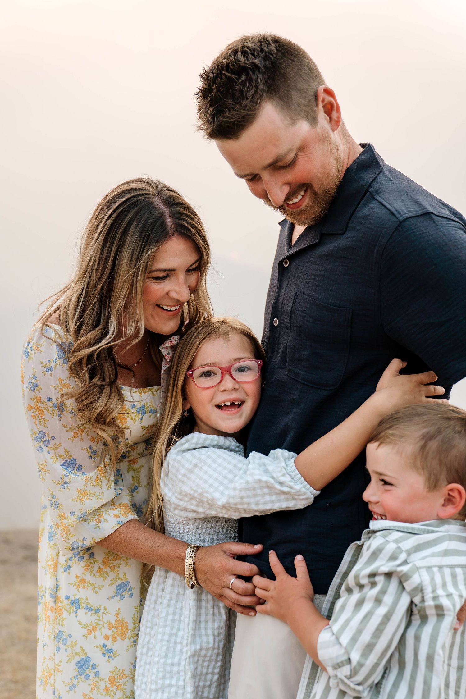 A happy family of four shares a joyful embrace outdoors, with two children hugging their smiling parents.