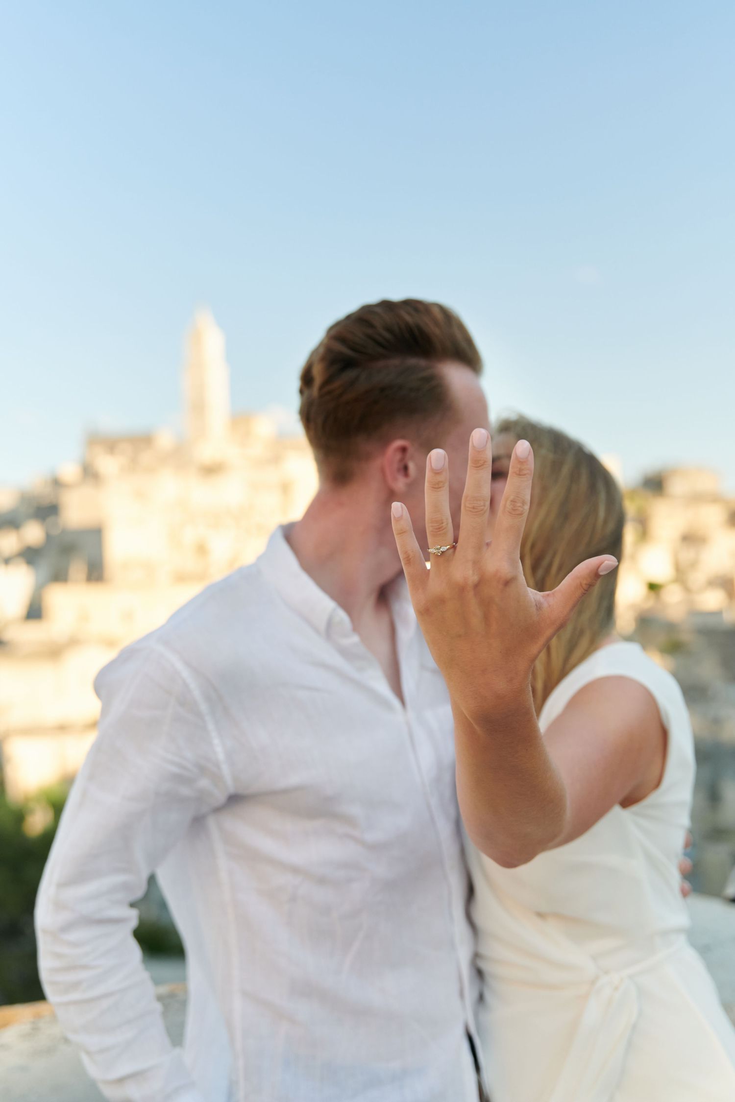 A romantic kiss captured against a scenic city backdrop at sunset.