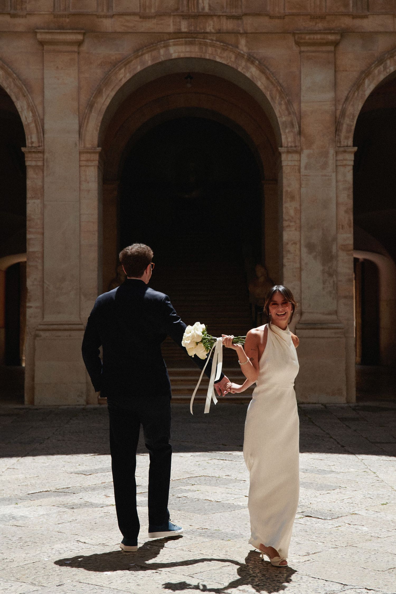Elegant wedding couple poses under historic stone archway.