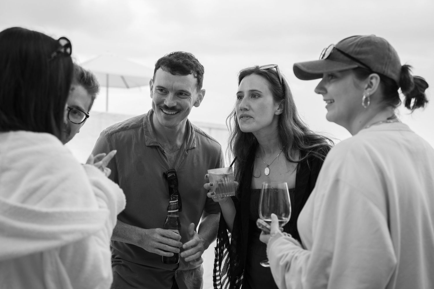 A group of people engaged in casual conversation while holding wine glasses outdoors.
