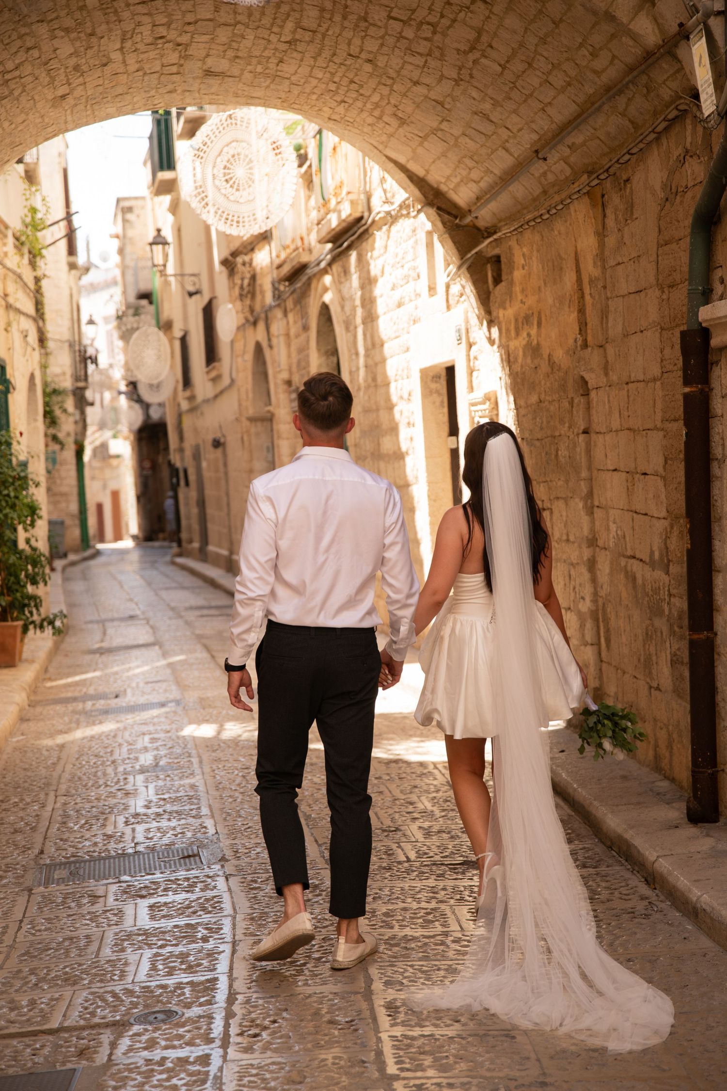 Newlyweds walk hand in hand through a charming Mediterranean alleyway.