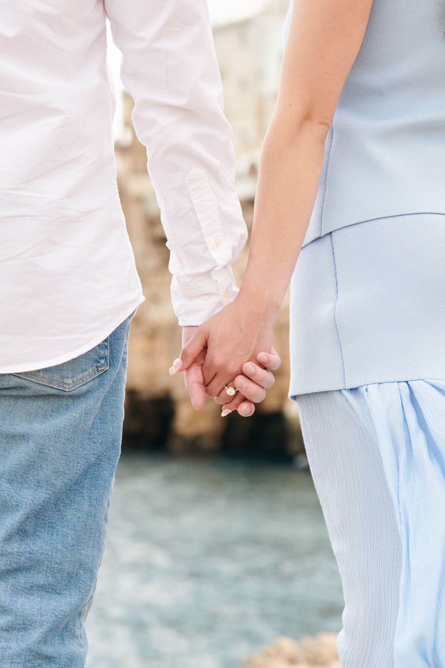 Close-up shot of two people holding hands in casual attire against a blurred background.
