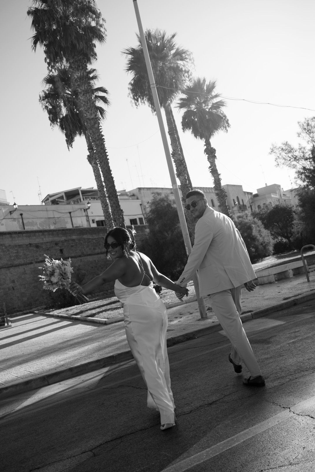 Black and white photo of people walking along a palm tree-lined path.