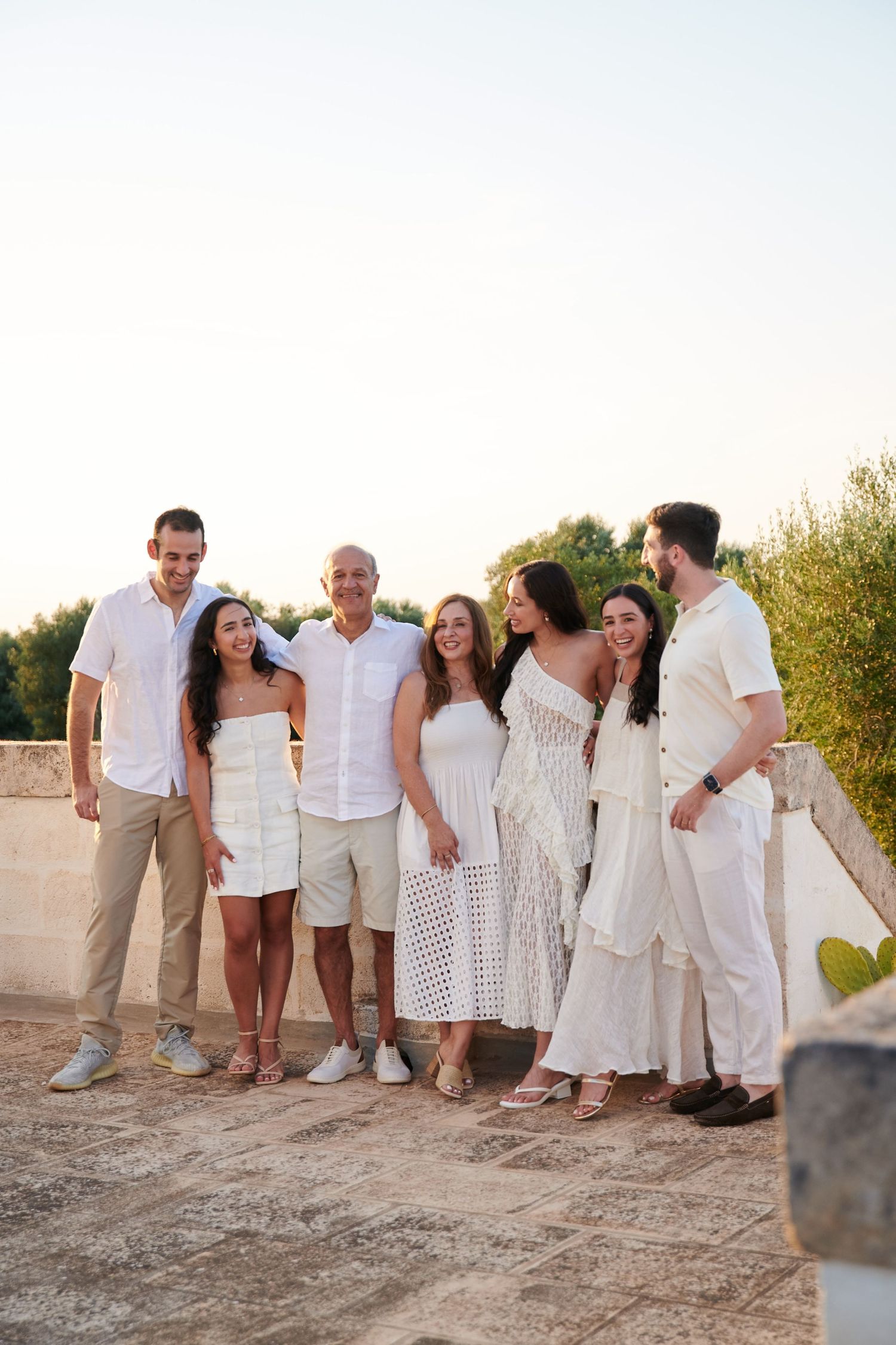 Group photo of people dressed in white and beige outfits posing together outdoors.