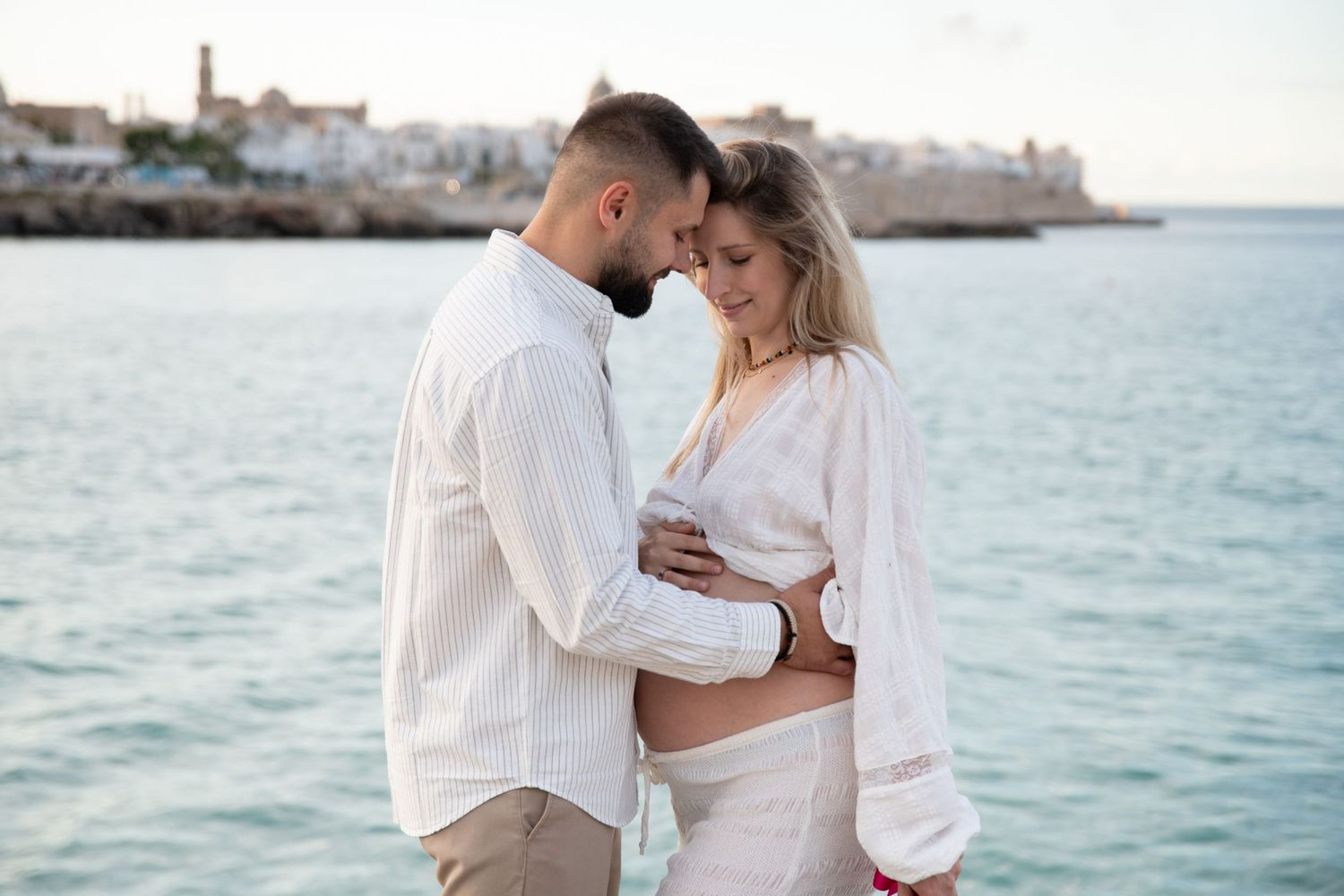 Romantic couple in white embracing against a Mediterranean seascape.
