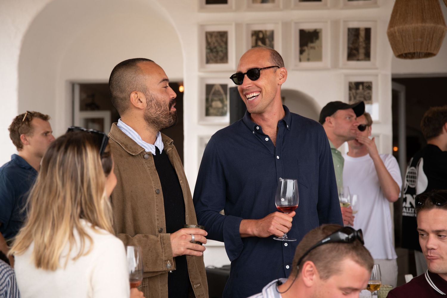 People enjoying drinks and conversation at an indoor social gathering with framed artwork on the walls.