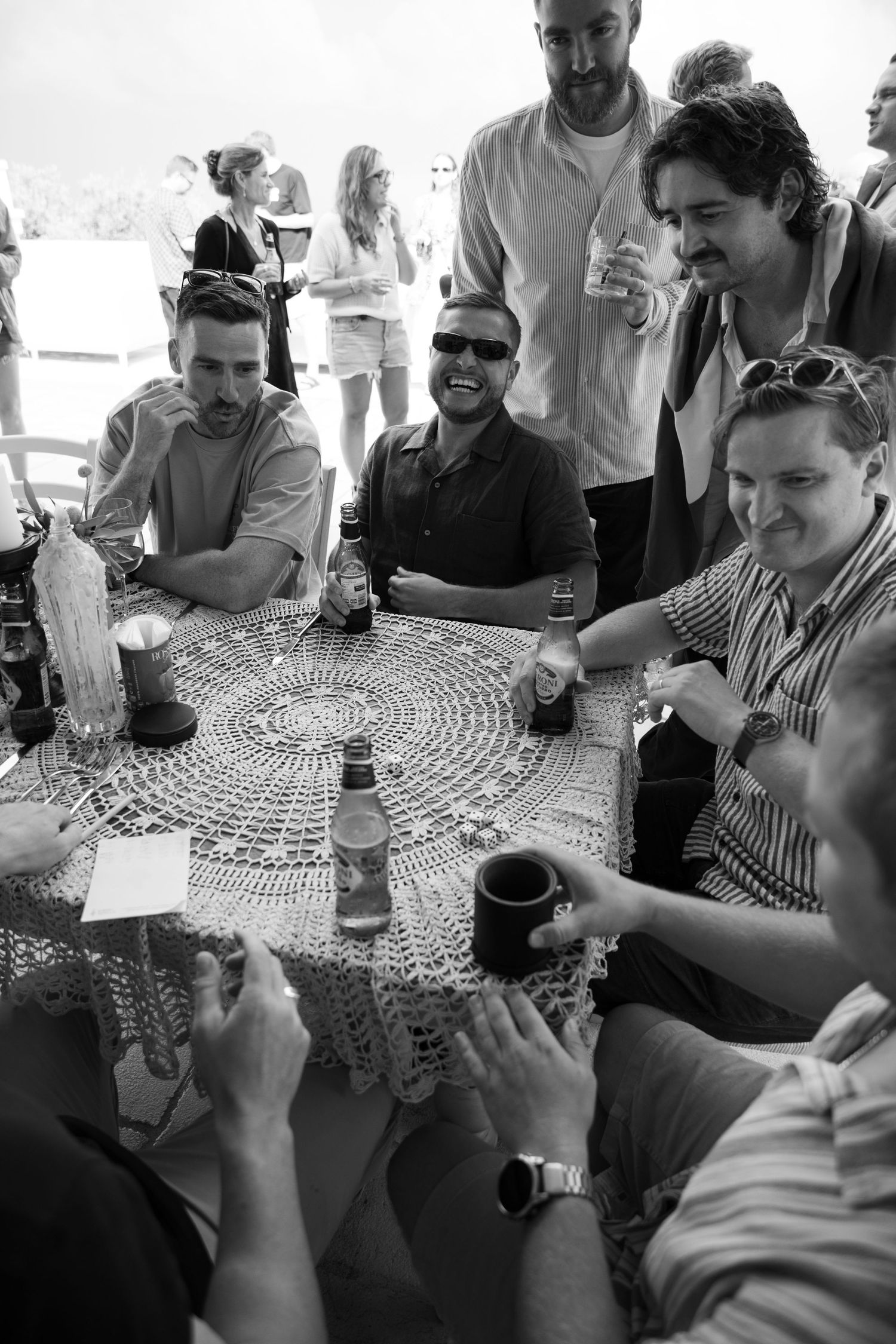 Friends gathered around a table with a lace tablecloth enjoying drinks and conversation.
