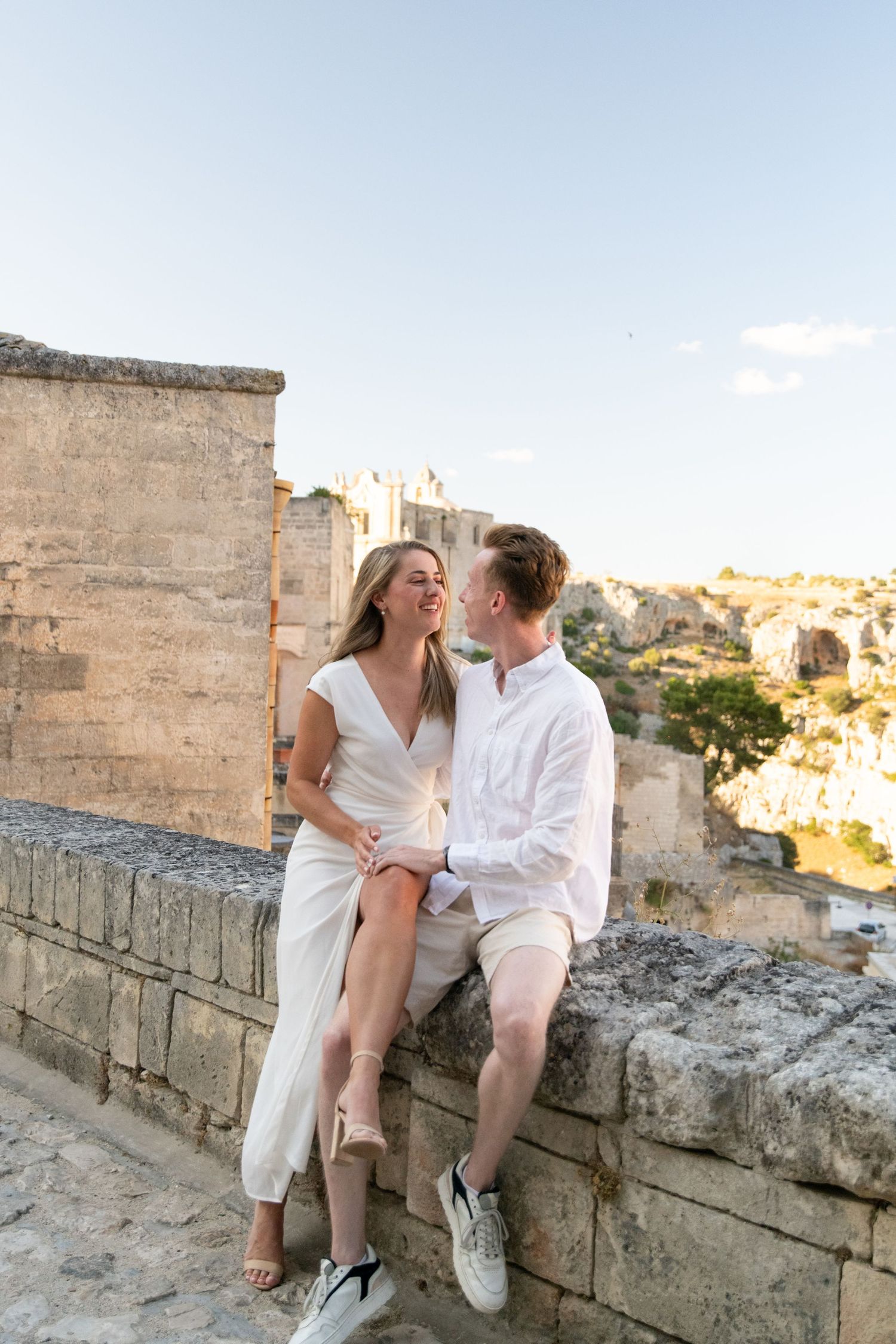 Couple sharing a romantic moment on an ancient stone wall overlooking a city.