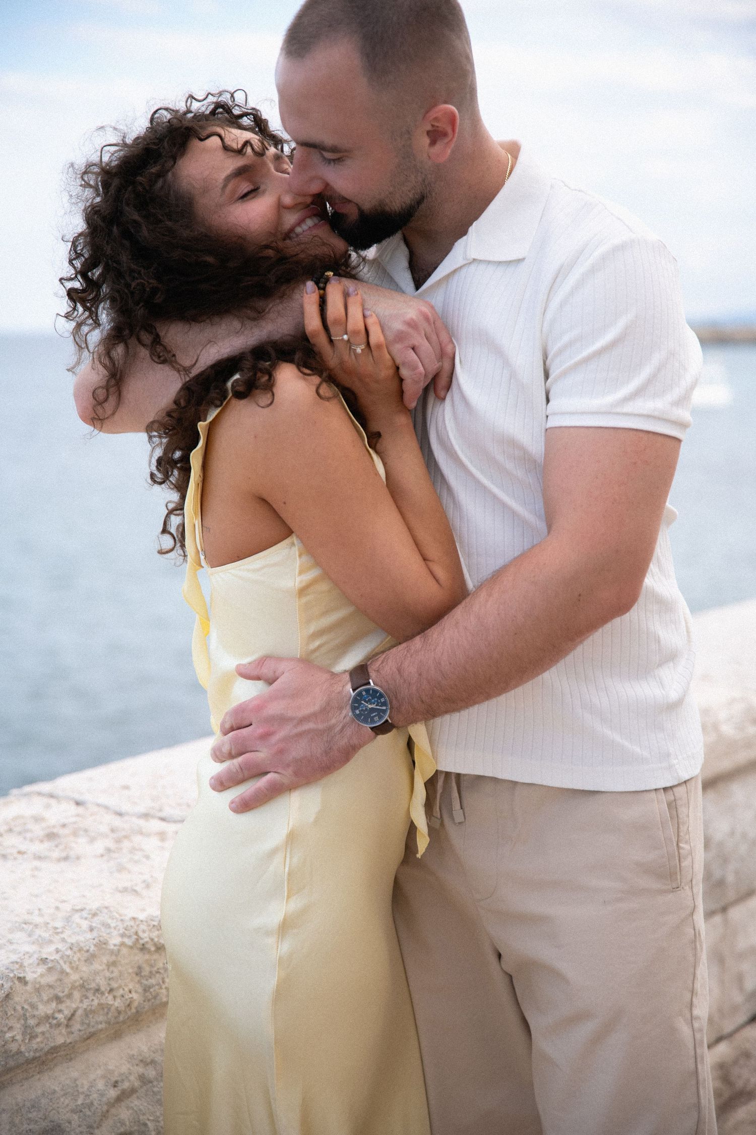 Couple in light summer attire sharing romantic moments by the Mediterranean seaside.