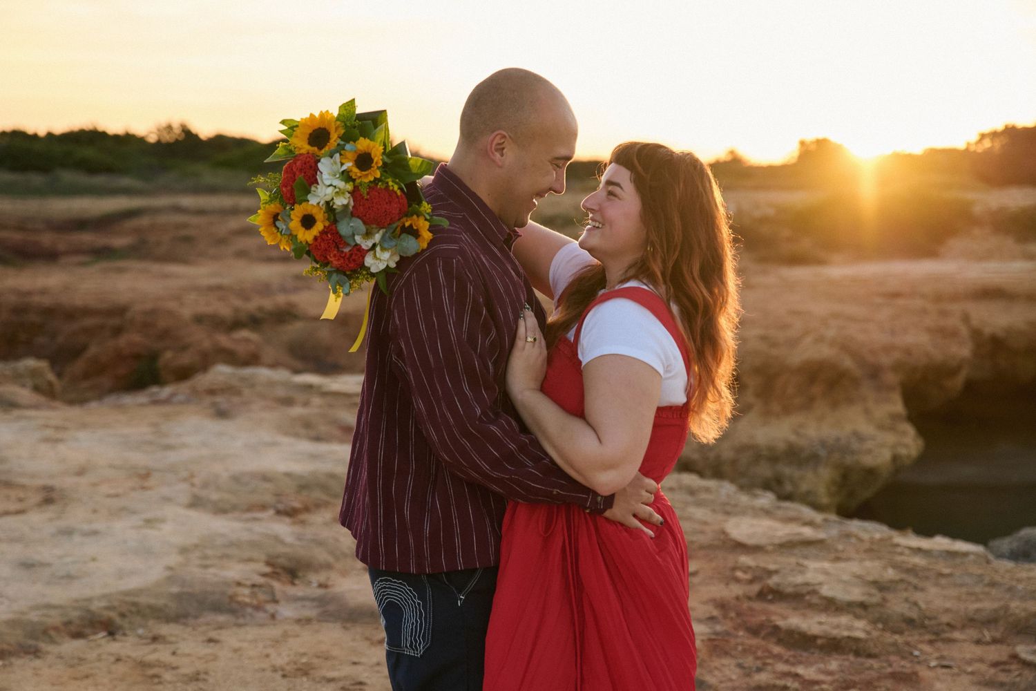 A couple embracing at sunset with sunflowers against a desert landscape.