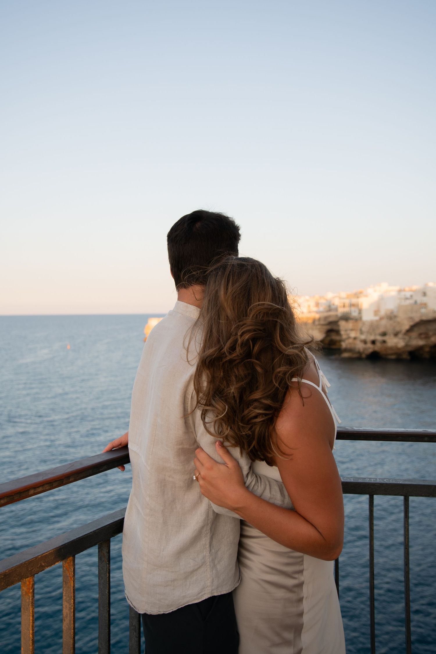 Couple embracing while watching sunset over Mediterranean Sea from coastal viewpoint.
